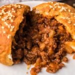 A baked meat bun split open, revealing a savory ground beef filling on a white plate—just like Air Fryer Unsloppy Joes Biscuit Pockets for an easy, not so sloppy sloppy joes twist.