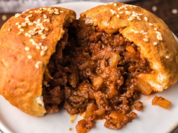 A baked meat bun split open, revealing a savory ground beef filling on a white plate—just like Air Fryer Unsloppy Joes Biscuit Pockets for an easy, not so sloppy sloppy joes twist.