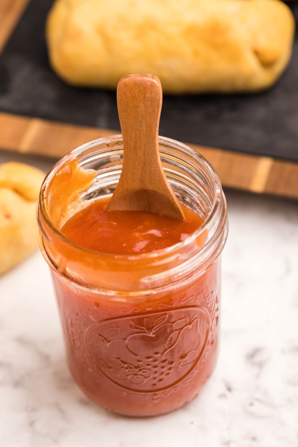 A glass jar of orange jam with a wooden spoon inside, on a marble surface—perfect for those seeking a hint of sweetness, just like sugar free sweet and sour sauce.