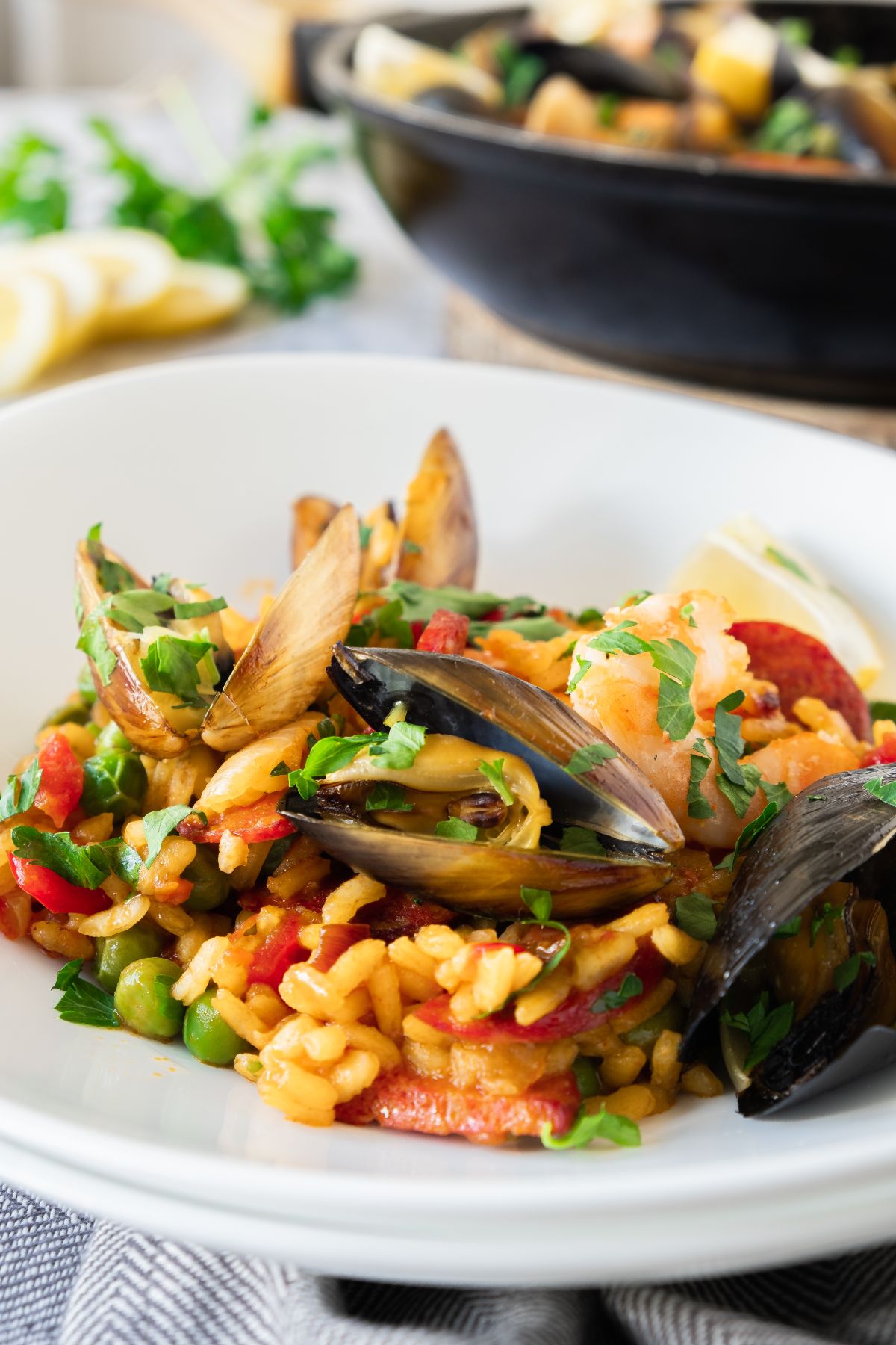 A plate of traditional Spanish paella with mussels, shrimp, peas, and rice, garnished with fresh parsley.