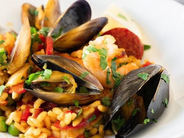 A plate of traditional Spanish paella with mussels, shrimp, rice, peas, and chopped parsley.