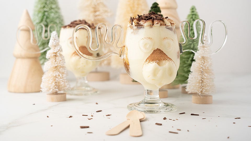 Two glasses of Tiramisu Cheesecake Mini Trifles in front of a christmas tree.
