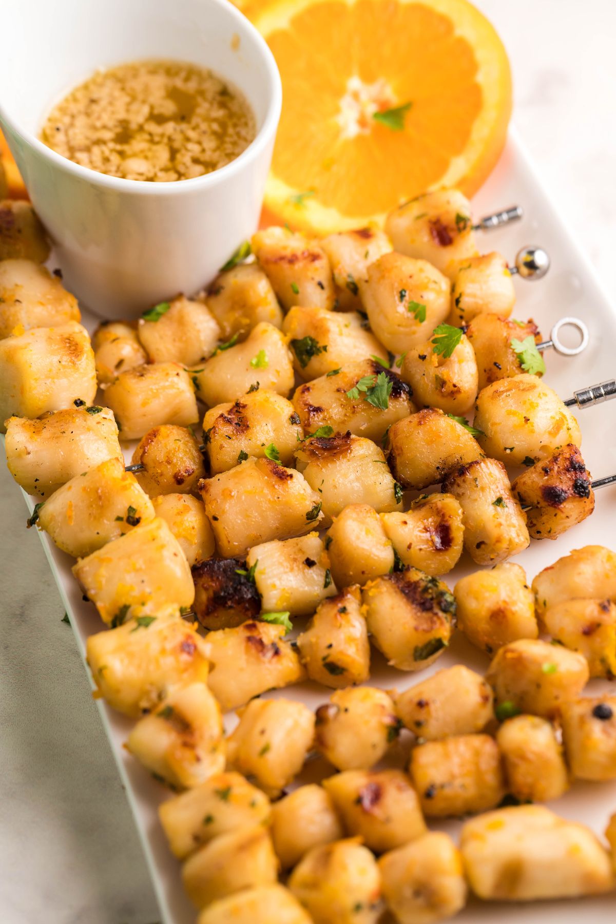 Grilled scallop skewers on a plate with orange slices and a cup of Citrus Garlic Smoked Butter Sauce—perfect seafood kabobs on the grill for any occasion.