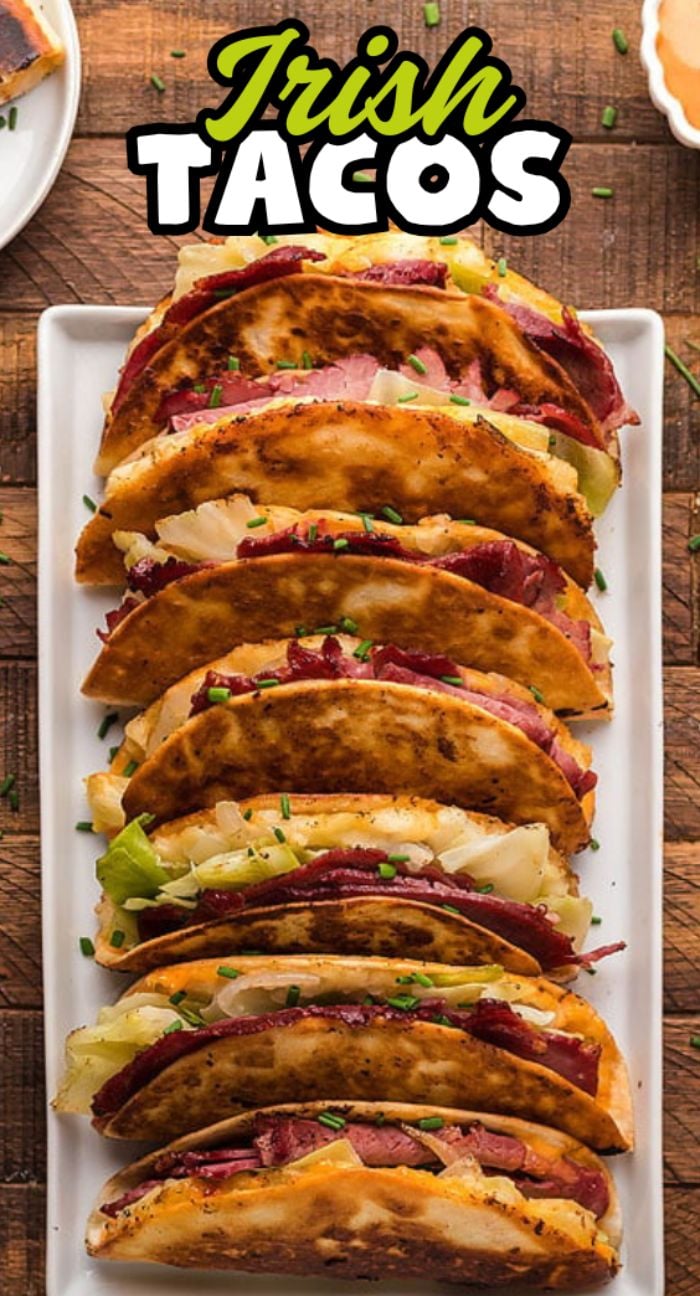 Six crispy Irish Tacos filled with corned beef, cabbage and onions, and potatoes, served on a rectangular white plate.