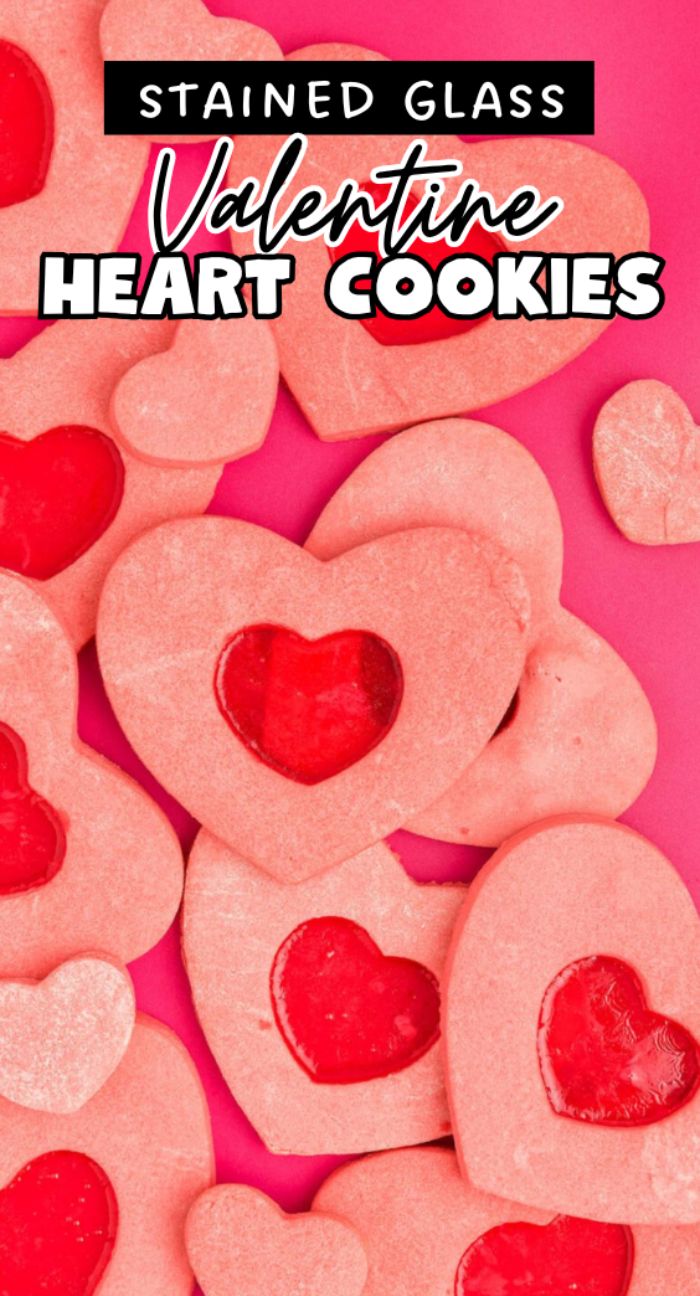 A pile of pink heart shaped sugar cookies, some featuring candy windows made with Jolly Ranchers or other hard candy.