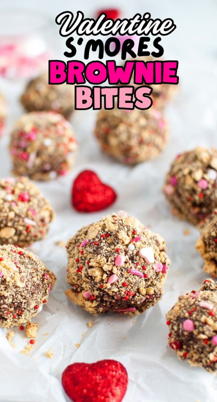 Brownie bites made using a boxed brownie mix, coated in crumbs and pink sprinkles with red heart decorations—an easy Valentine treat on white parchment paper.
