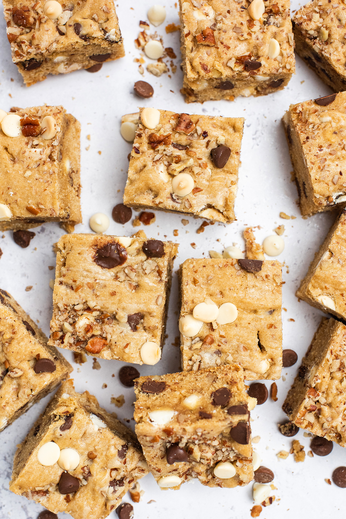 Squares of Double Chocolate Pecan Blondies with semisweet and white chocolate chips scattered on a white surface.