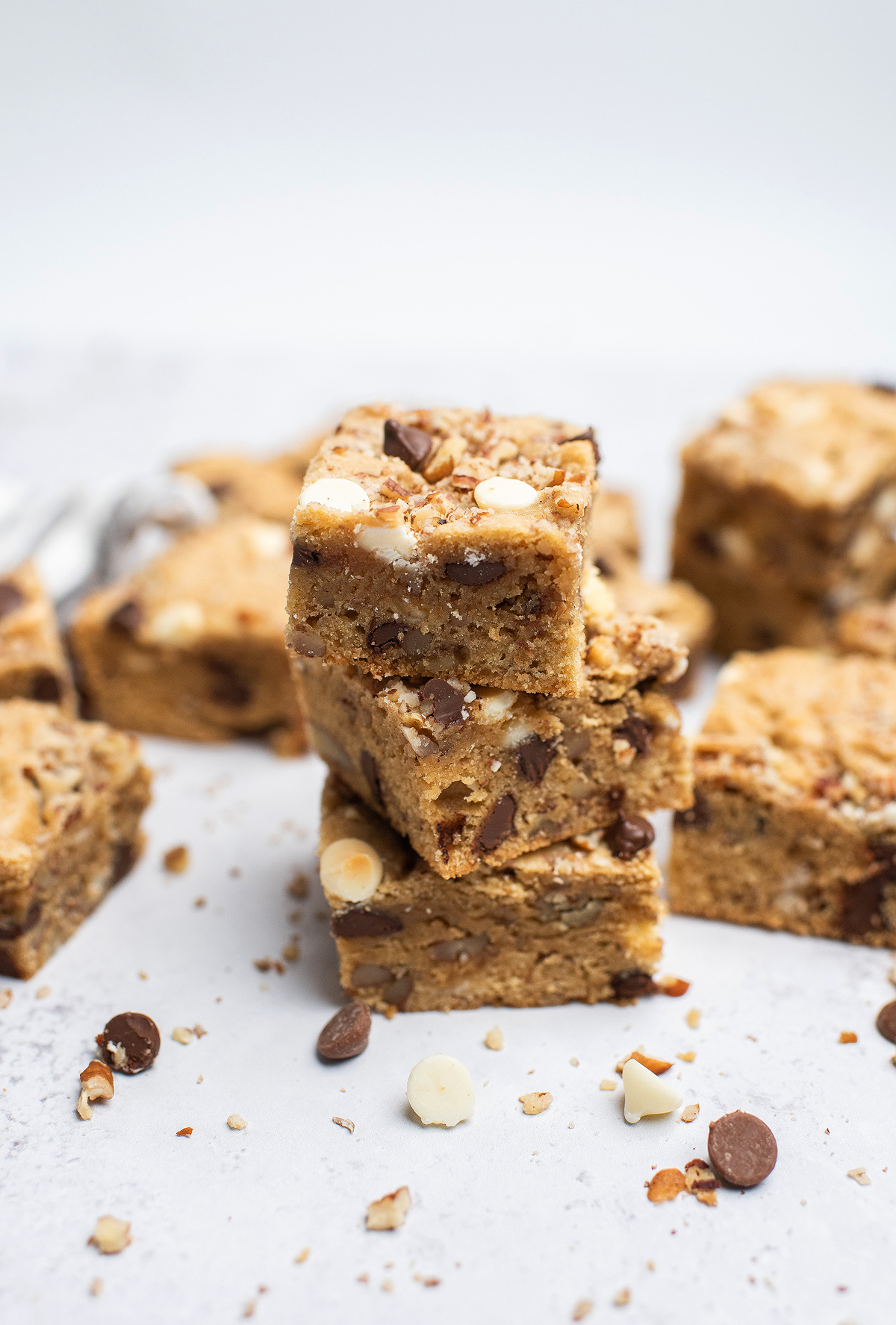 A stack of blondie bars with chocolate chips and white chocolate chips on a white surface, these blonde brownies offer a delicious twist for any sweet tooth.