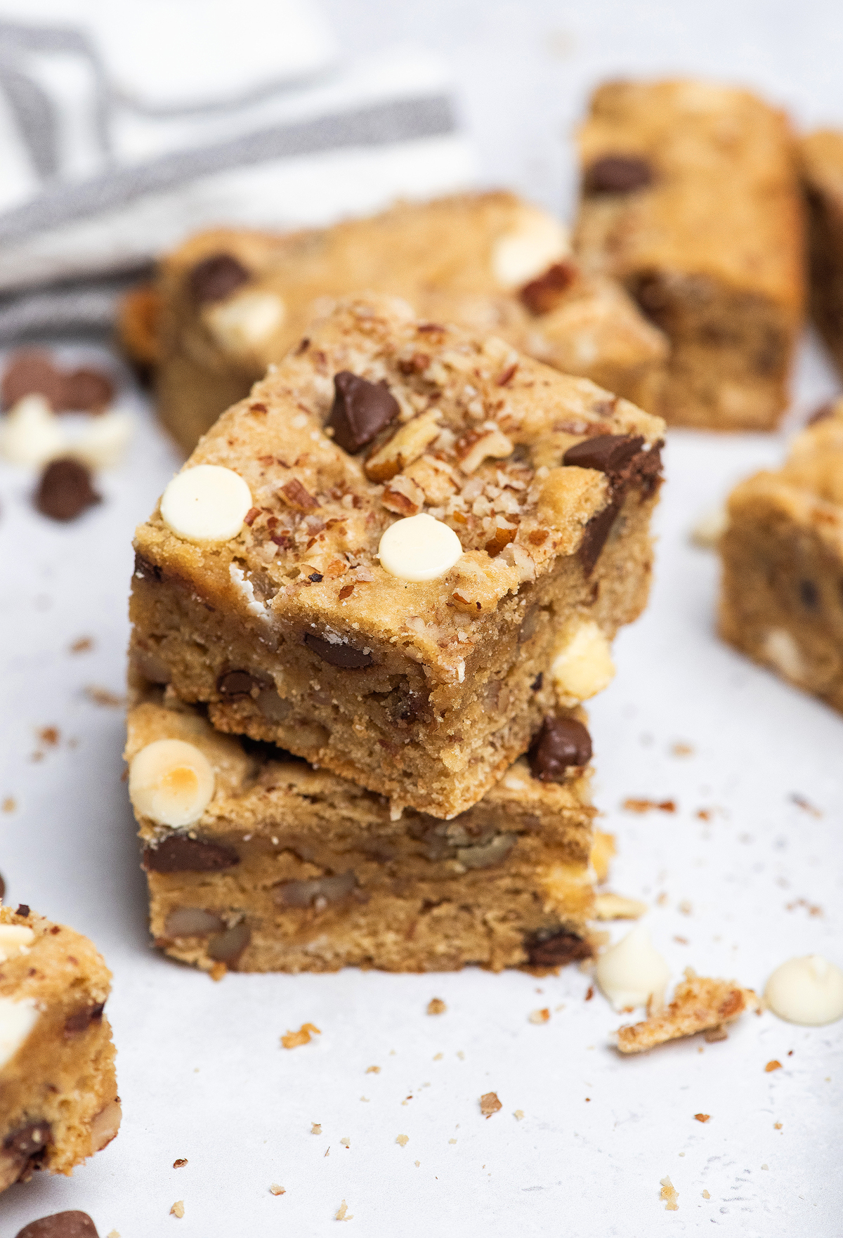 Three stacked Double Chocolate Pecan Blondies, loaded with semisweet and white chocolate chips, rest on a white surface.
