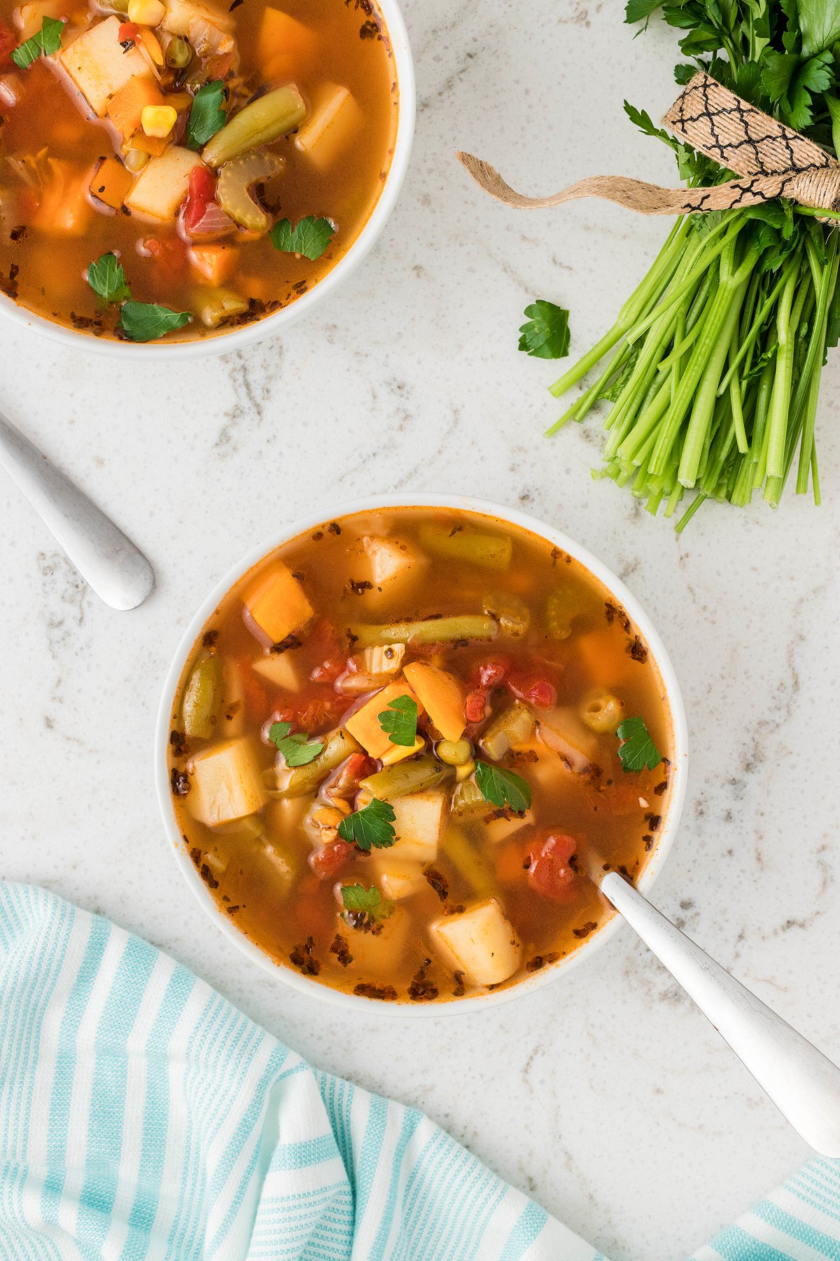 Two bowls of Instant Pot Vegetable Soup on a white surface with fresh parsley and a striped kitchen towel nearby, perfect for anyone seeking an easy vegan soup recipe.