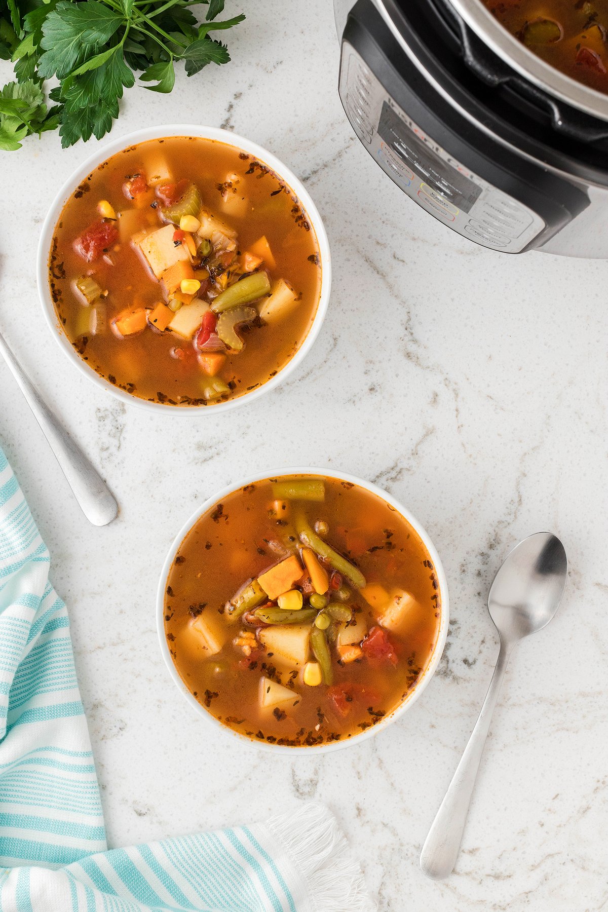 Two bowls of Instant Pot Vegetable Soup on a white counter with spoons, a striped towel, and an Instant Pot nearby—perfect for making soup in an Instant Pot or pressure cooker for a quick 30 minute meal.