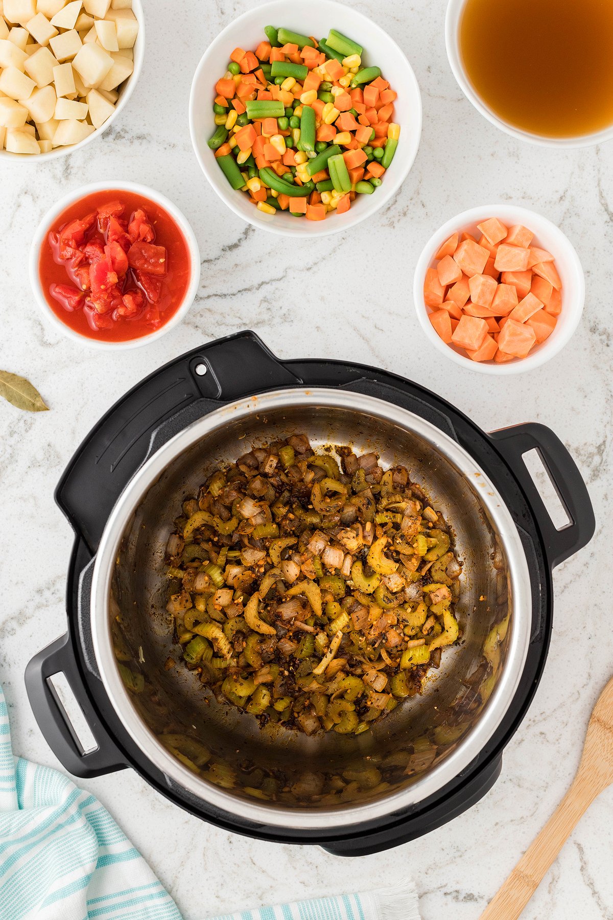 Top view of sautéed onions and celery in an Instant Pot, surrounded by bowls of broth and chopped vegetables—perfect for a quick 30 Minute Meal or as the base for an easy Instant Pot Vegetable Soup.