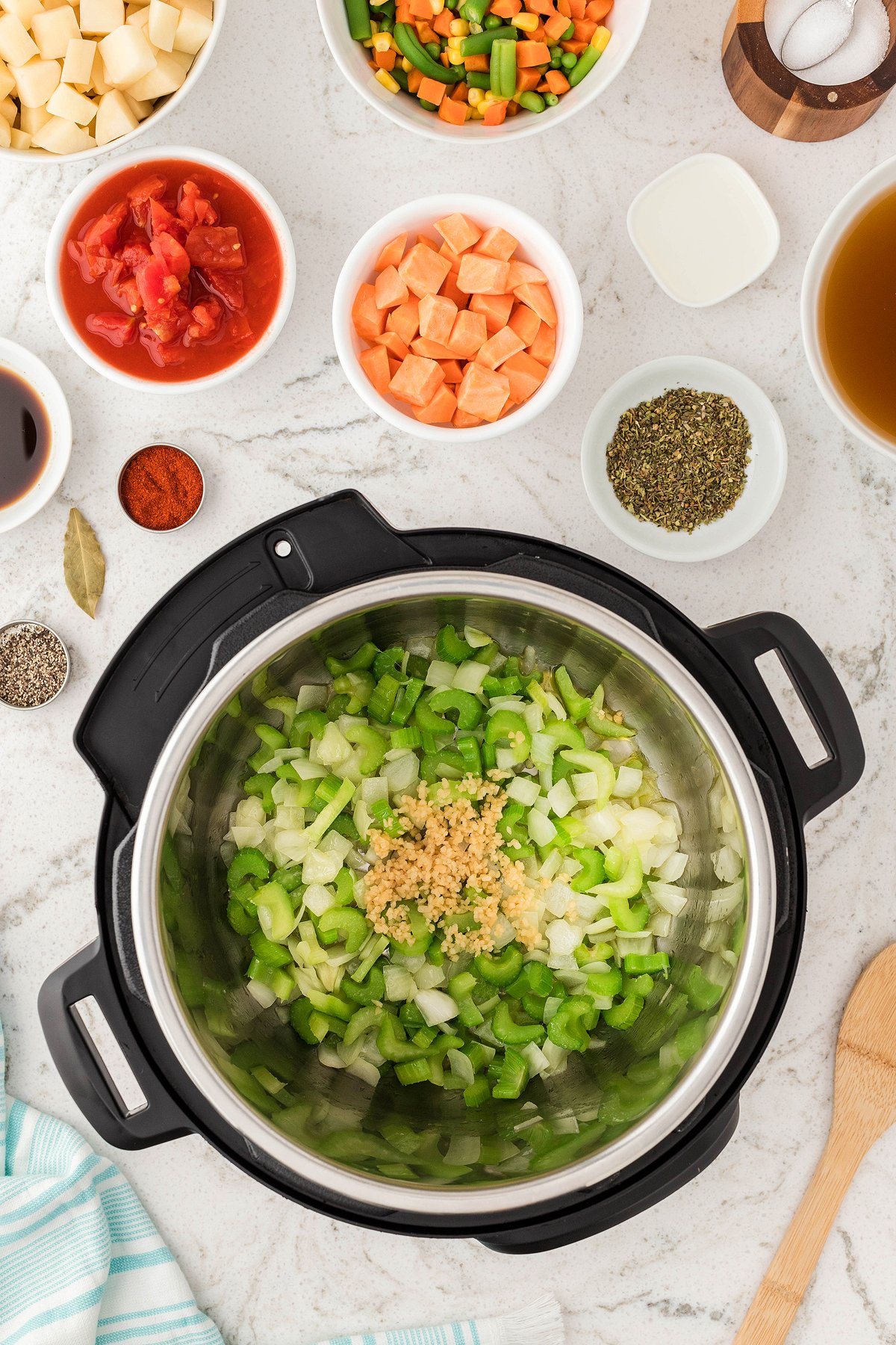 Chopped onions, celery, and garlic in an Instant Pot set the stage for an Instant Pot Vegetable Soup, surrounded by bowls of fresh and frozen vegetables and seasonings—perfect for a quick vegetarian or vegan soup recipe.