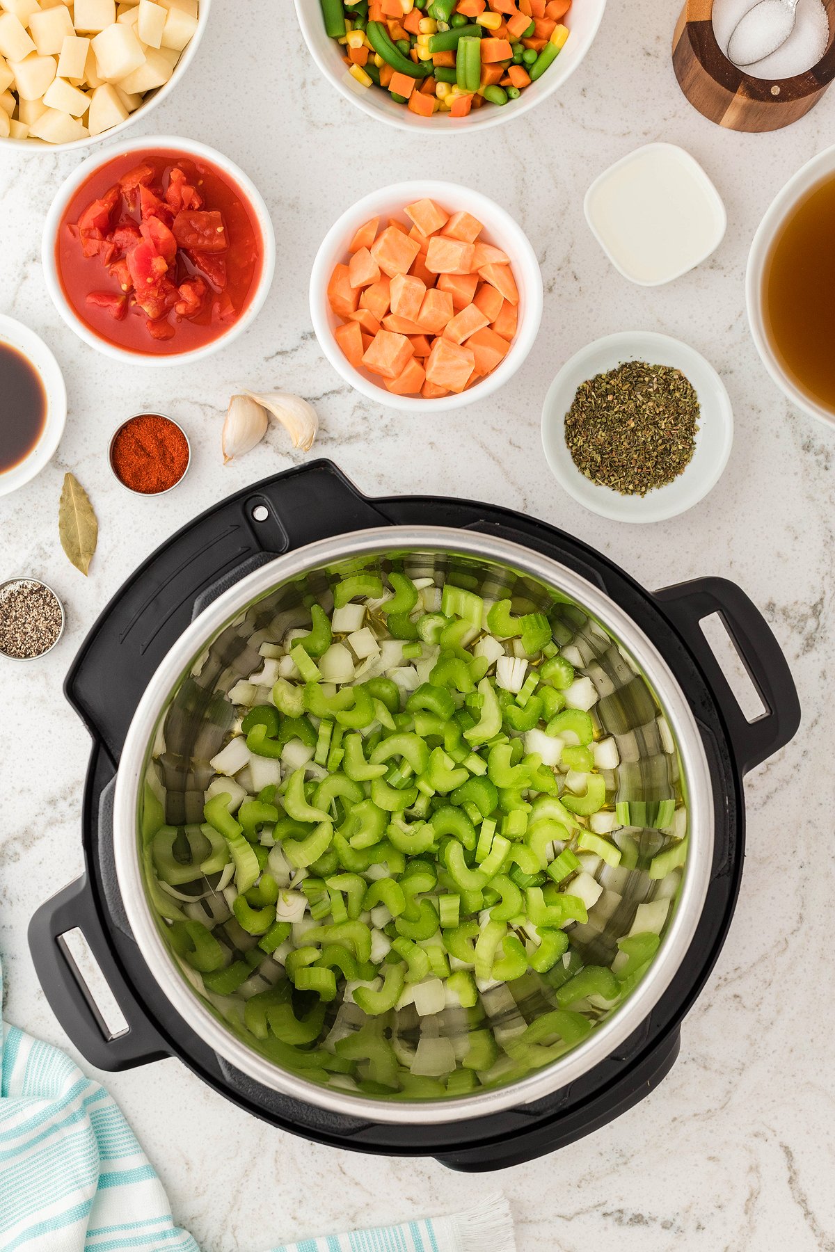 Chopped celery and onion in an Instant Pot, surrounded by bowls of vegetables, spices, and broth—perfect for making a hearty Instant Pot Vegetable Soup or your favorite vegetarian soup recipe.