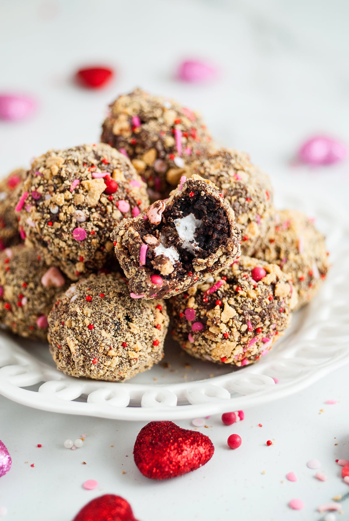 A plate of chocolate truffles coated in sprinkles, with one truffle showing a creamy filling inside—an easy Valentine treat that's just as delightful as making Valentine S'mores Brownie Bites using a boxed brownie mix.