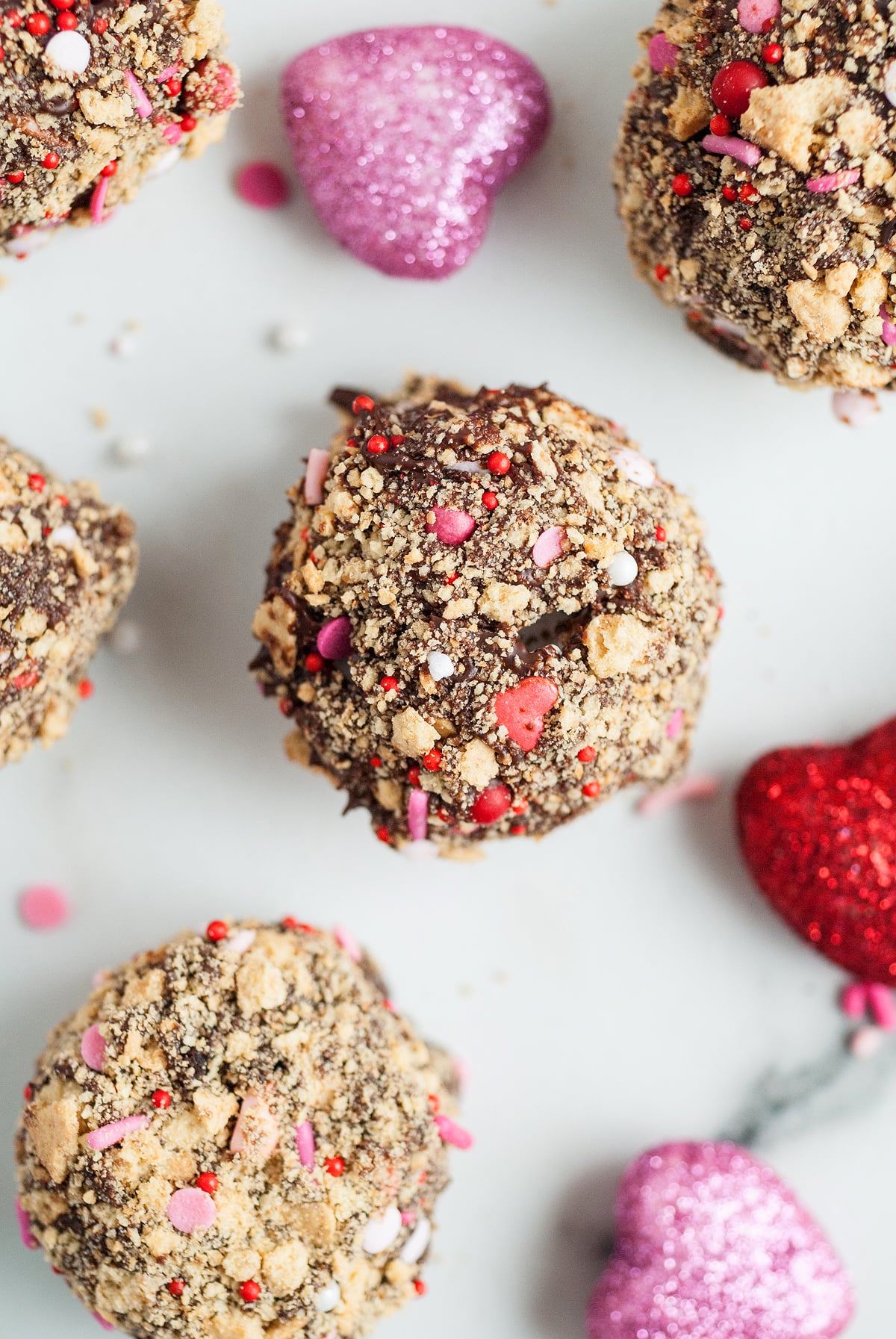 S’more truffles coated with sprinkles and crumbs, surrounded by glittery red and pink heart decorations—an easy Valentine treat using a boxed brownie mix.