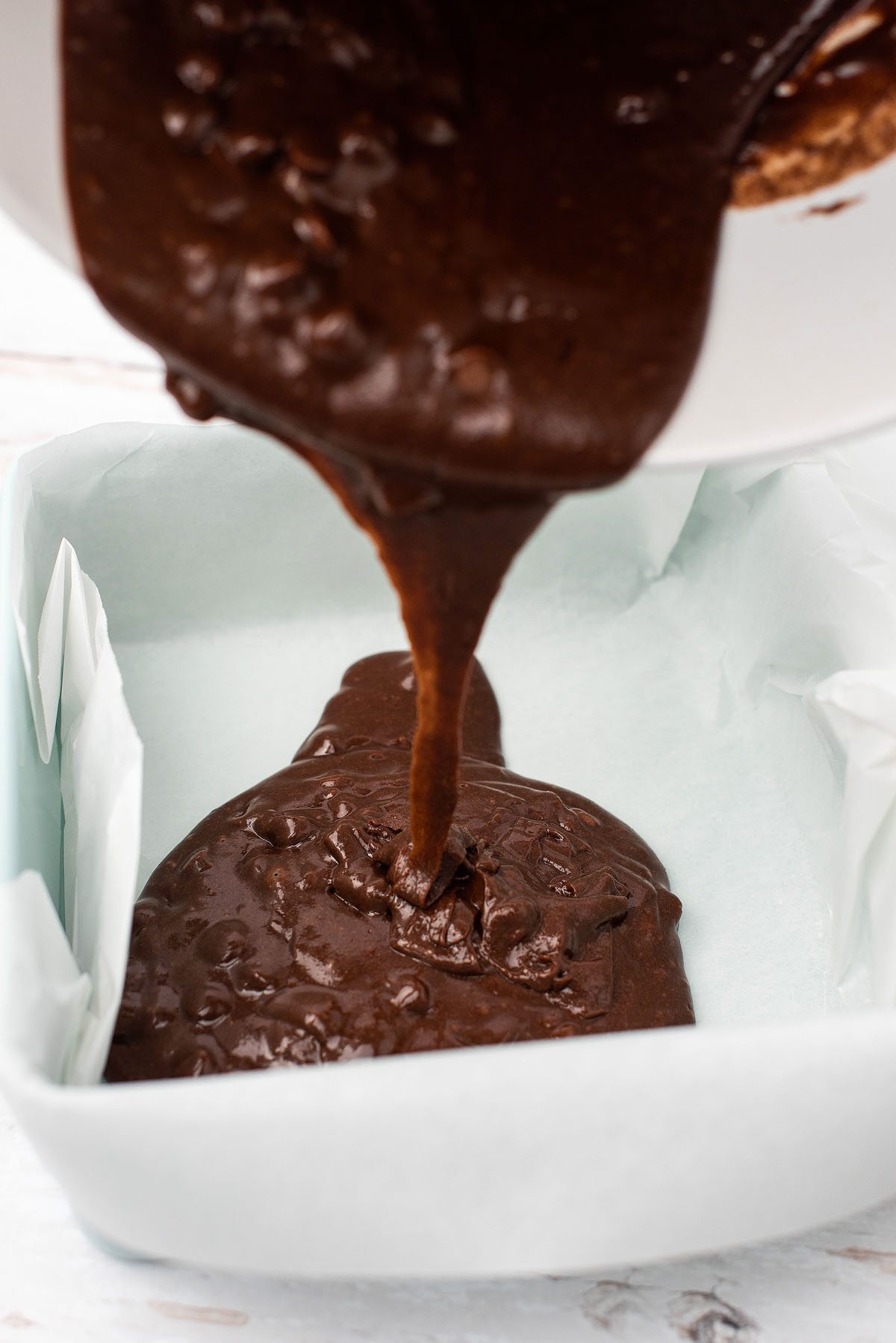 Thick chocolate brownie batter being poured into a parchment-lined baking pan, perfect for making Valentine Brownies—a sweet Valentine treat to share with someone special.