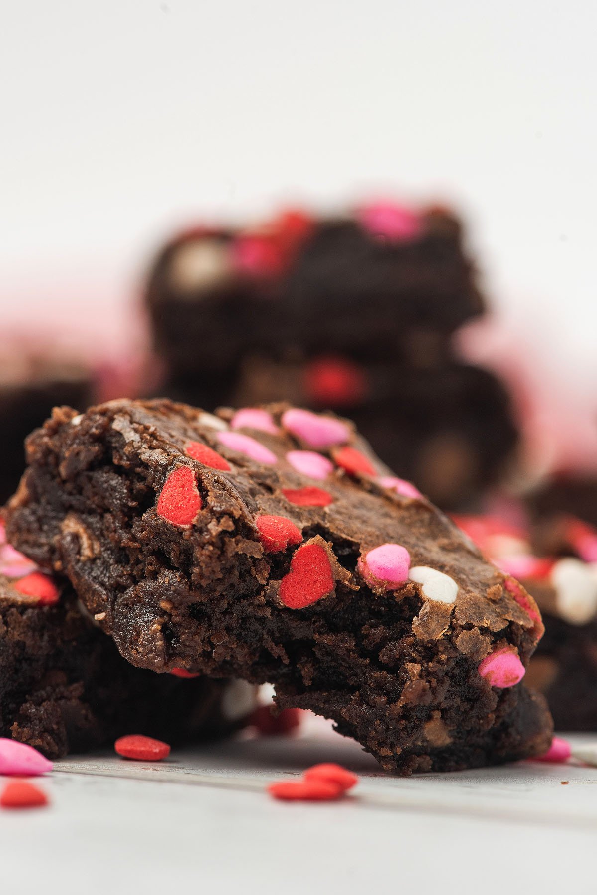 A chocolate brownie with a bite taken out, topped with red, pink, and white heart-shaped sprinkles—perfect as a sweet Valentine treat.