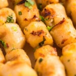 Close-up of golden-brown gnocchi garnished with herbs, paired with a Citrus Garlic Smoked Butter Sauce partially visible on the side.
