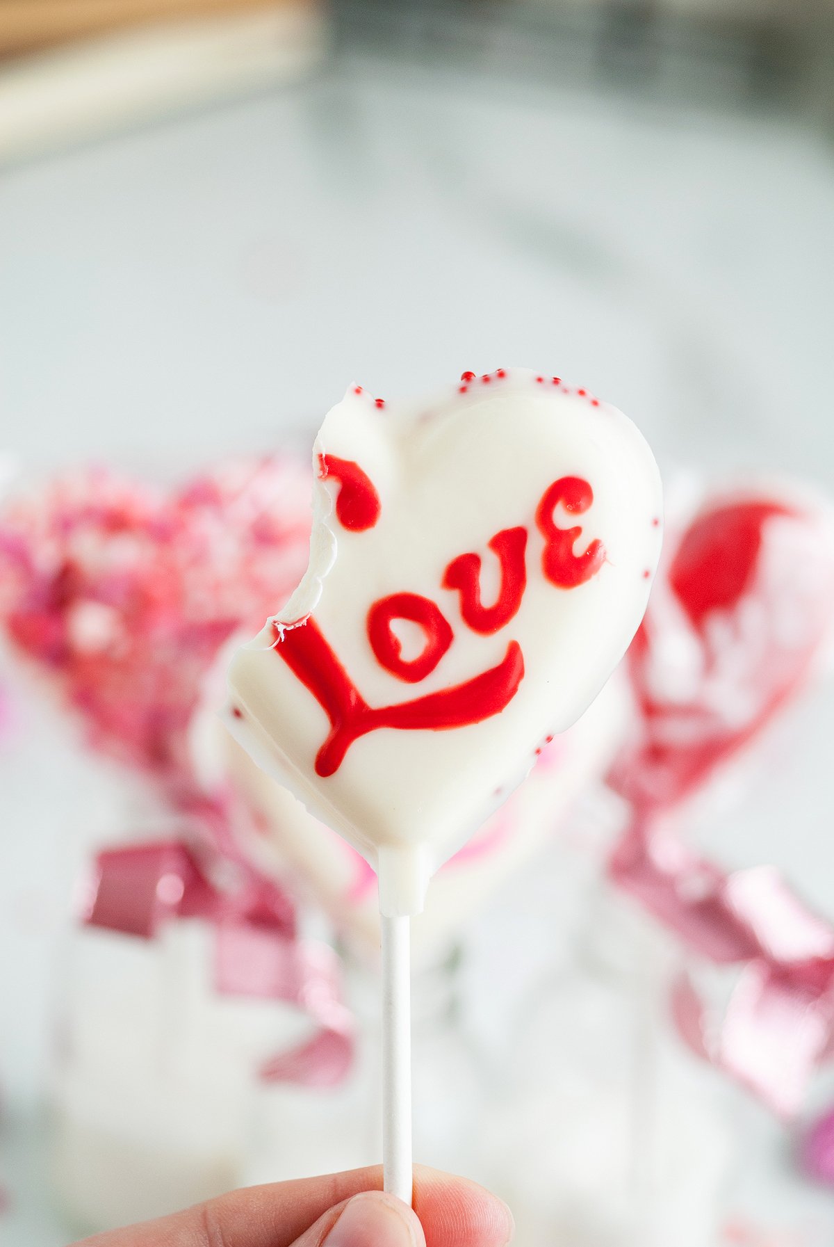 A heart-shaped white chocolate lollipop with "Love" written in red and a bite taken from the top—perfect for Valentine Lollipop Treats you can make using chocolate pops molds.