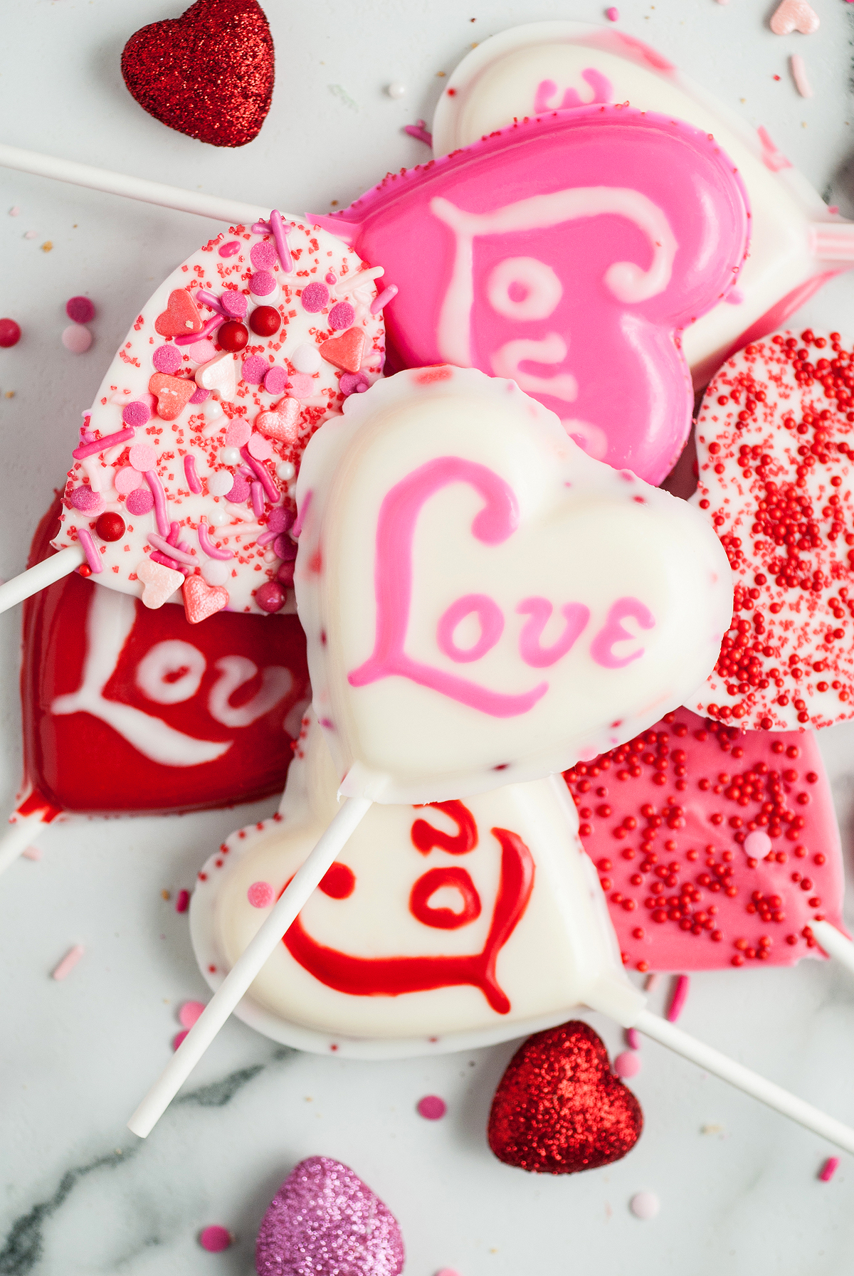 Heart-shaped cake pops with "Love" written on them, decorated in pink, red, and white sprinkles—perfect Valentine Lollipop Treats for your sweetheart or to inspire you to make chocolate lollipops with molds at home.