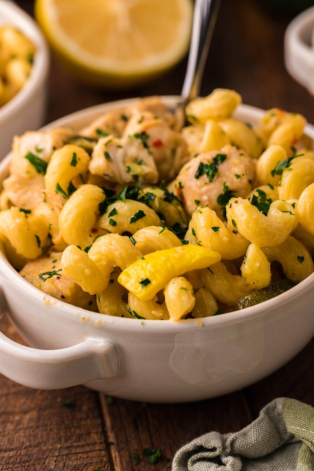 Curly pasta with creamy sauce, chicken, and parsley in a white bowl, with lemon in the background—perfect for Instant Pot Lemon Chicken Pasta lovers.