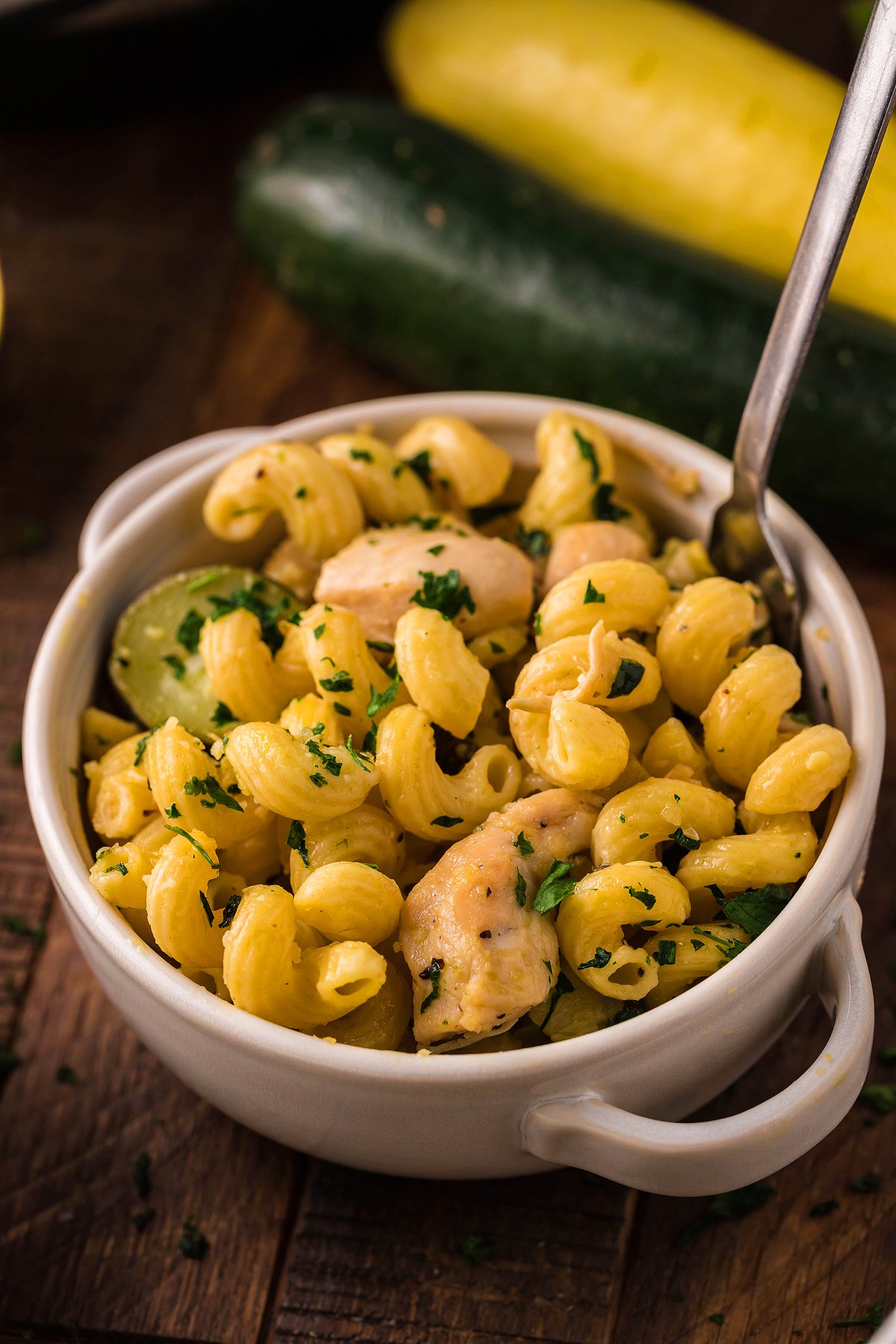 A bowl of Pasta with Zucchini and Squash and tender chicken, garnished with chopped herbs, sits on a wooden table—perfect for fans of Instant Pot Lemon Chicken Pasta.