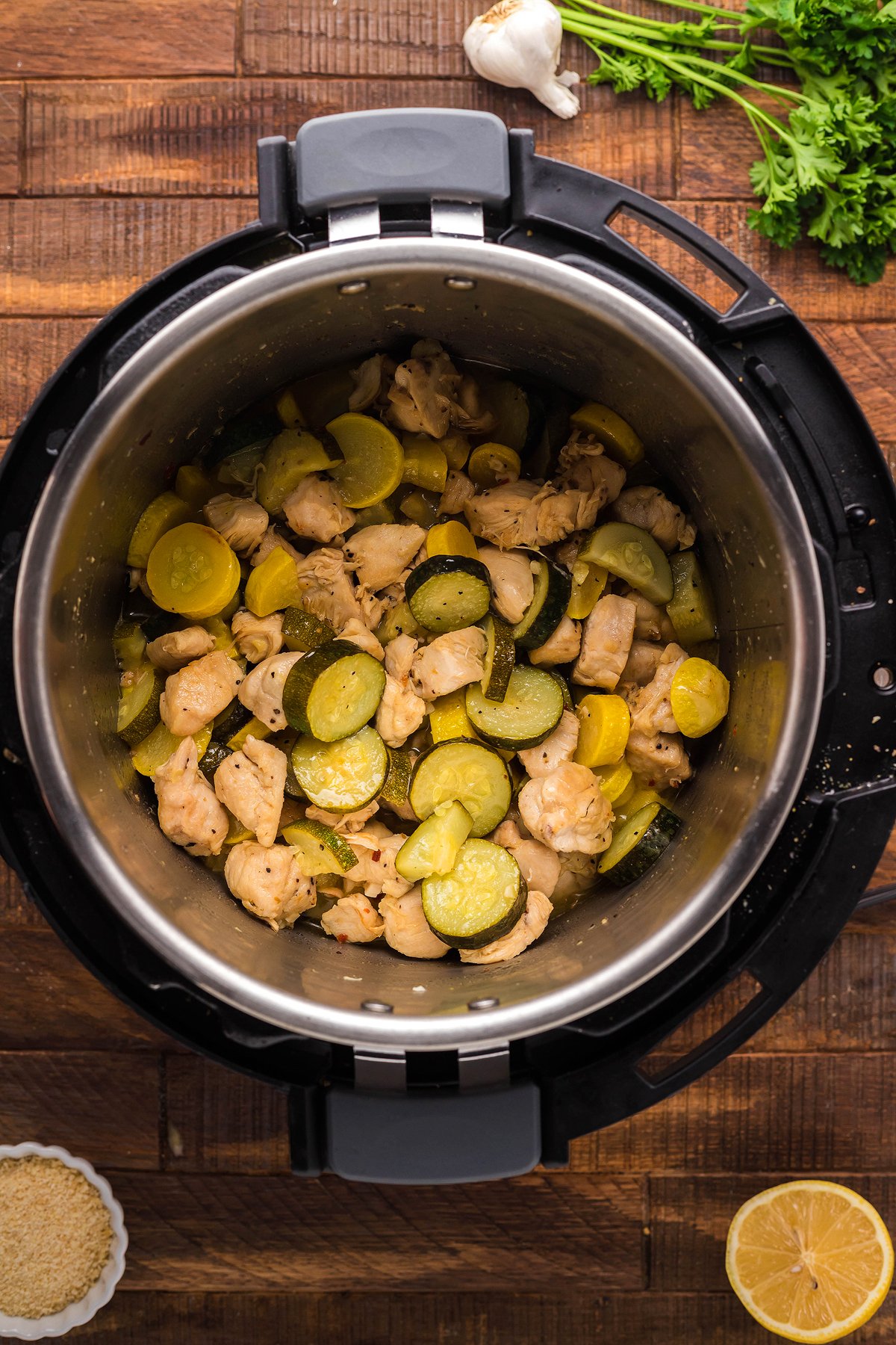 Chicken, zucchini, and yellow squash cooked in an Instant Pot on a wooden table with herbs and garlic nearby—perfect for making pasta with chicken and vegetables.