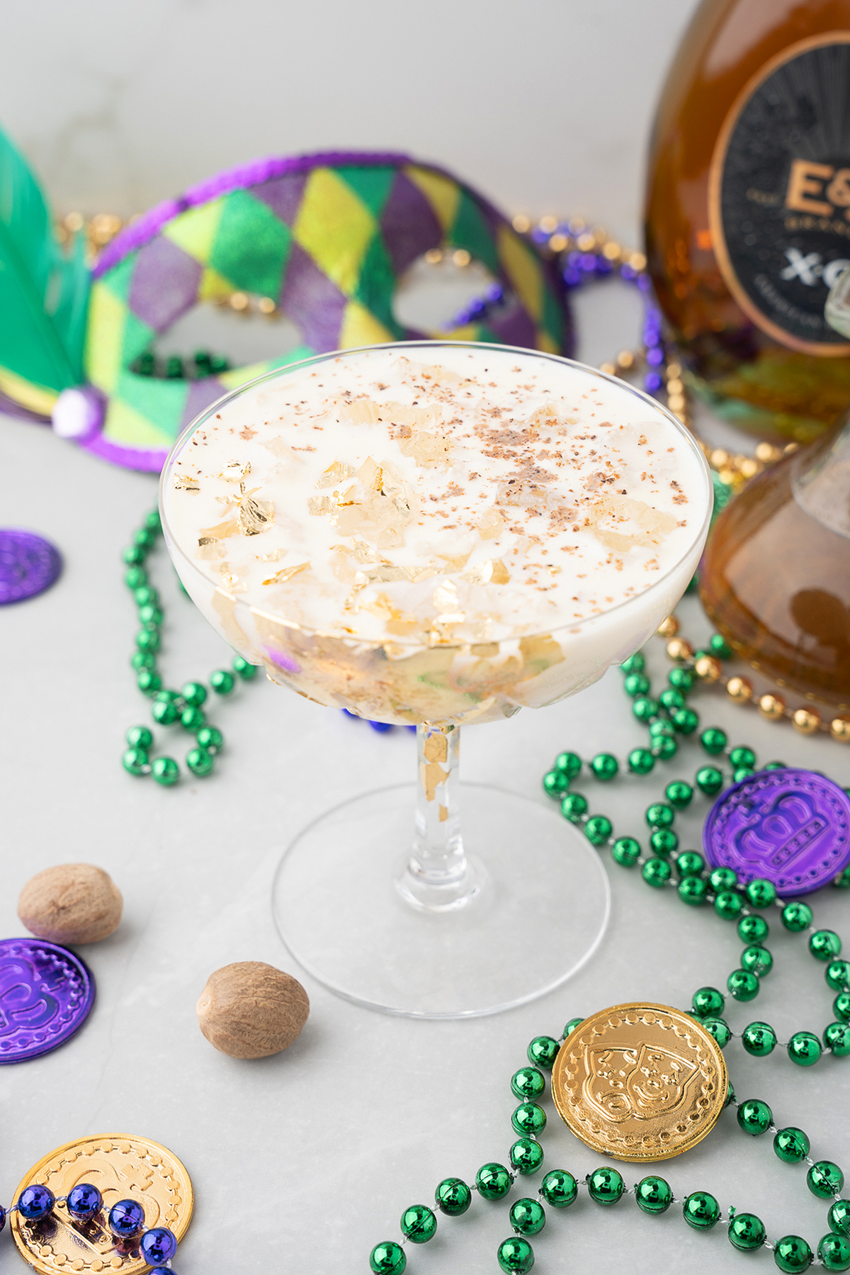 A cocktail garnished with gold flakes, surrounded by Mardi Gras beads, coins, and a festive mask—perfect for a Mardi Gras party with homemade vanilla bean simple syrup.