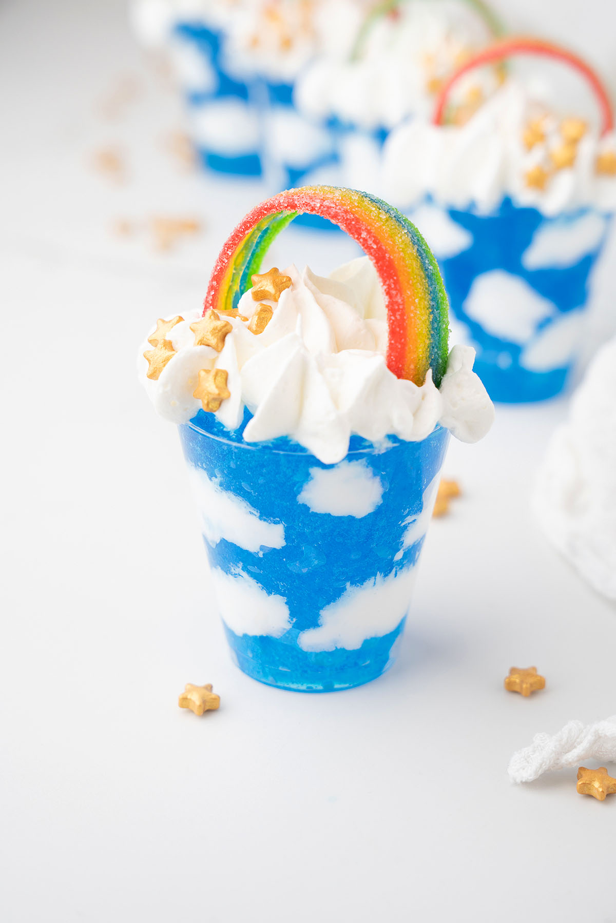 A blue cup with a rainbow on top, perfect for serving Rainbow Pot O' Gold Jello Vodka Shots at your next Pride Day or St. Patrick&rsquo;s Day celebration.