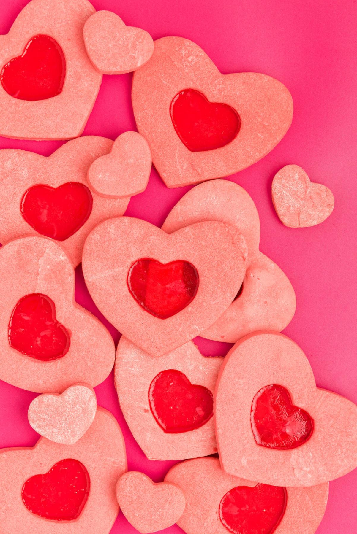 Heart-shaped sugar cookies with red centers, these stained glass heart cookies are displayed on a bright pink background.