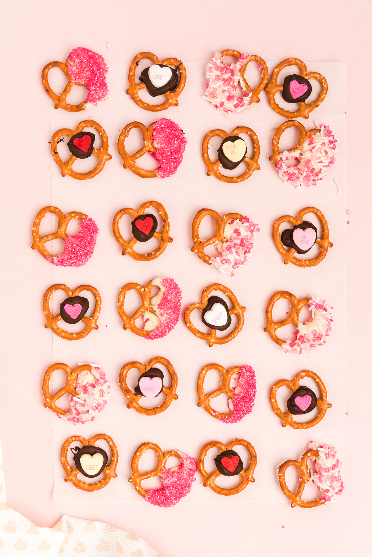Heart-shaped Valentine pretzels decorated with pink, red, and white sprinkles and candy hearts make the perfect Valentine’s Day treat on parchment paper.