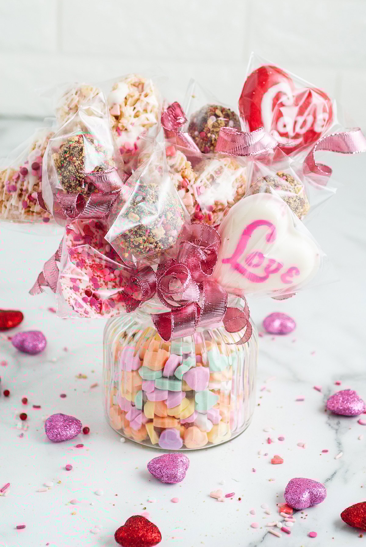 A jar filled with candy hearts holds wrapped, homemade Valentine’s treats tied with pink ribbons—a perfect Valentine’s Day Homemade Treat Box.