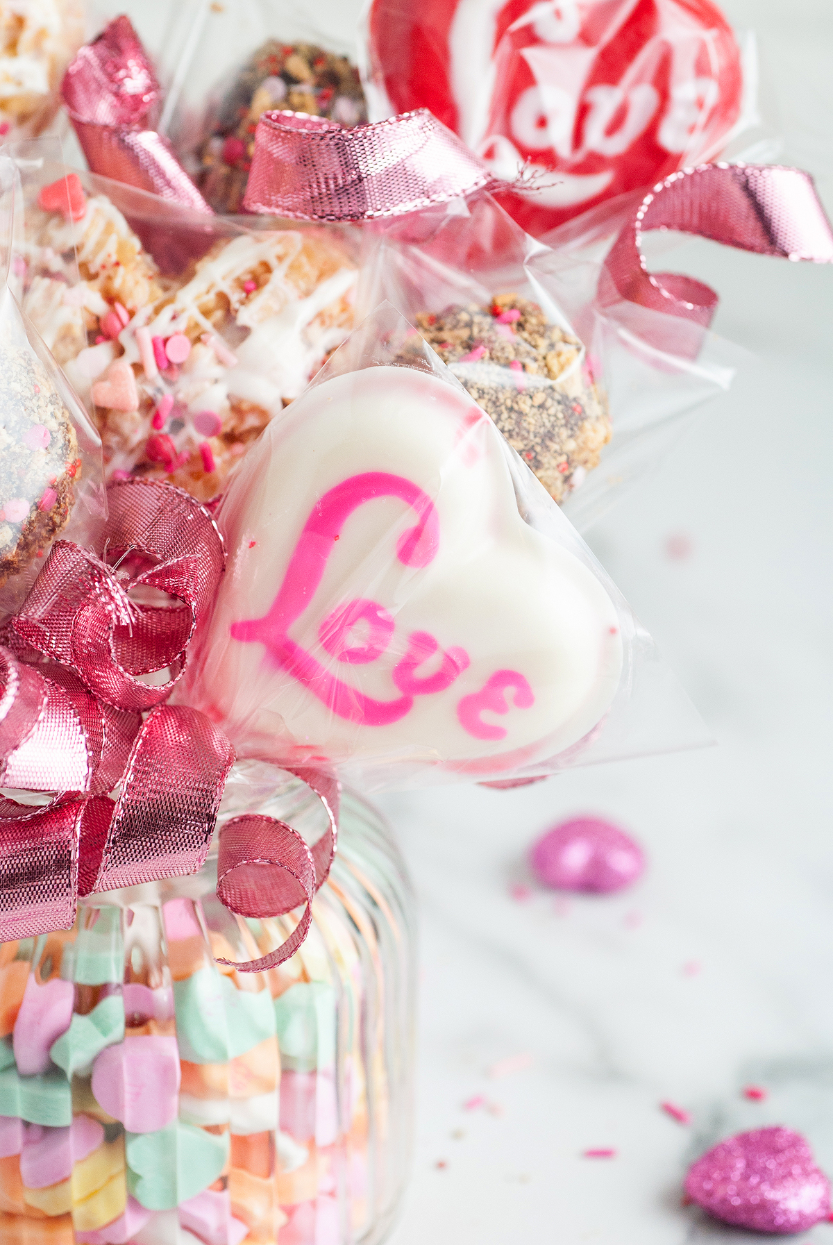 Heart-shaped white chocolate with "Love" written in pink, wrapped with a pink ribbon among colorful treats—perfect for a Valentine’s sweets gift box or to add charm to any Valentine's Day Homemade Treat Box.