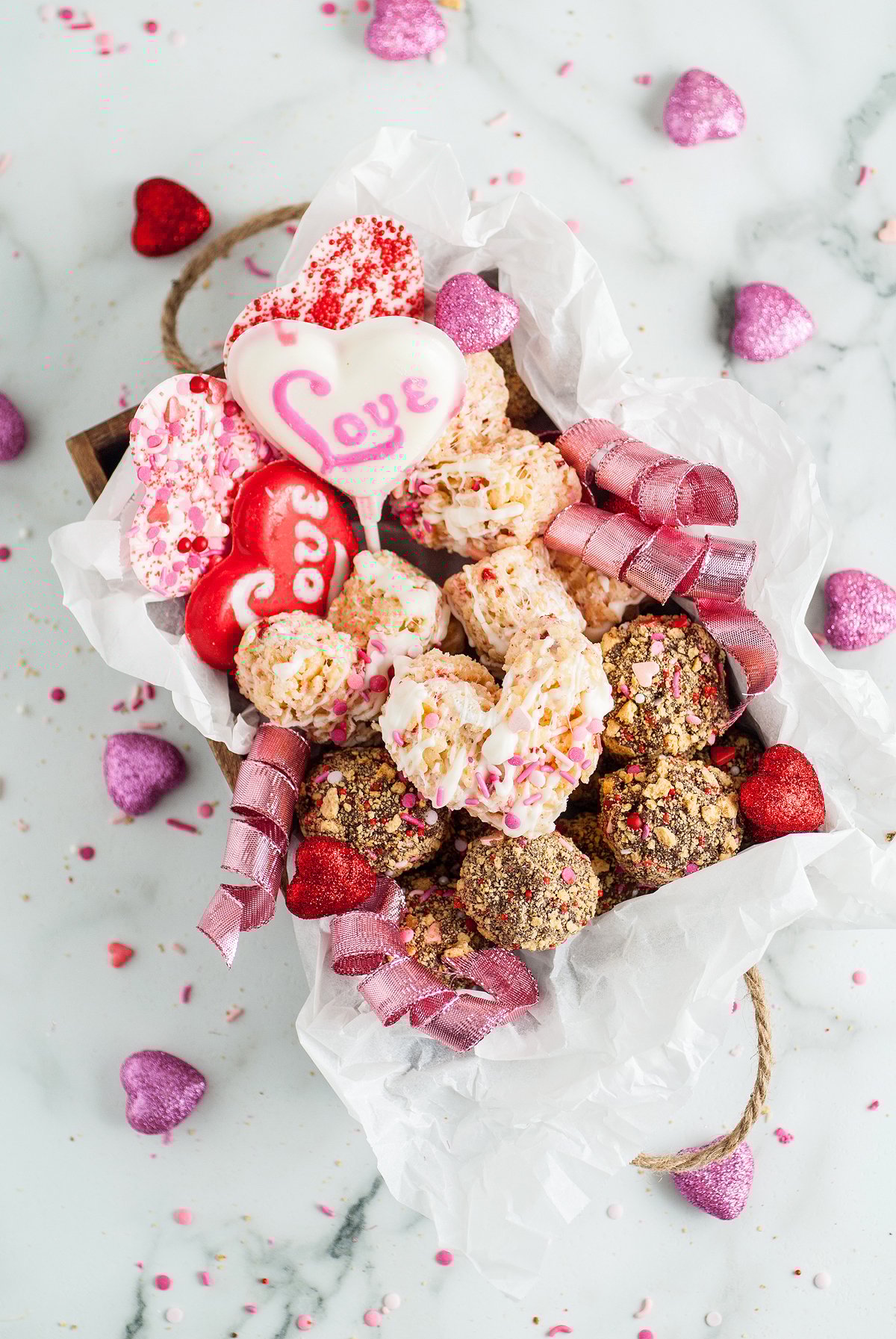 A valentine’s sweets gift box with heart-shaped cookies, truffles, and pink decorations sits on a marble surface—a perfect way to share homemade Valentine’s treats.