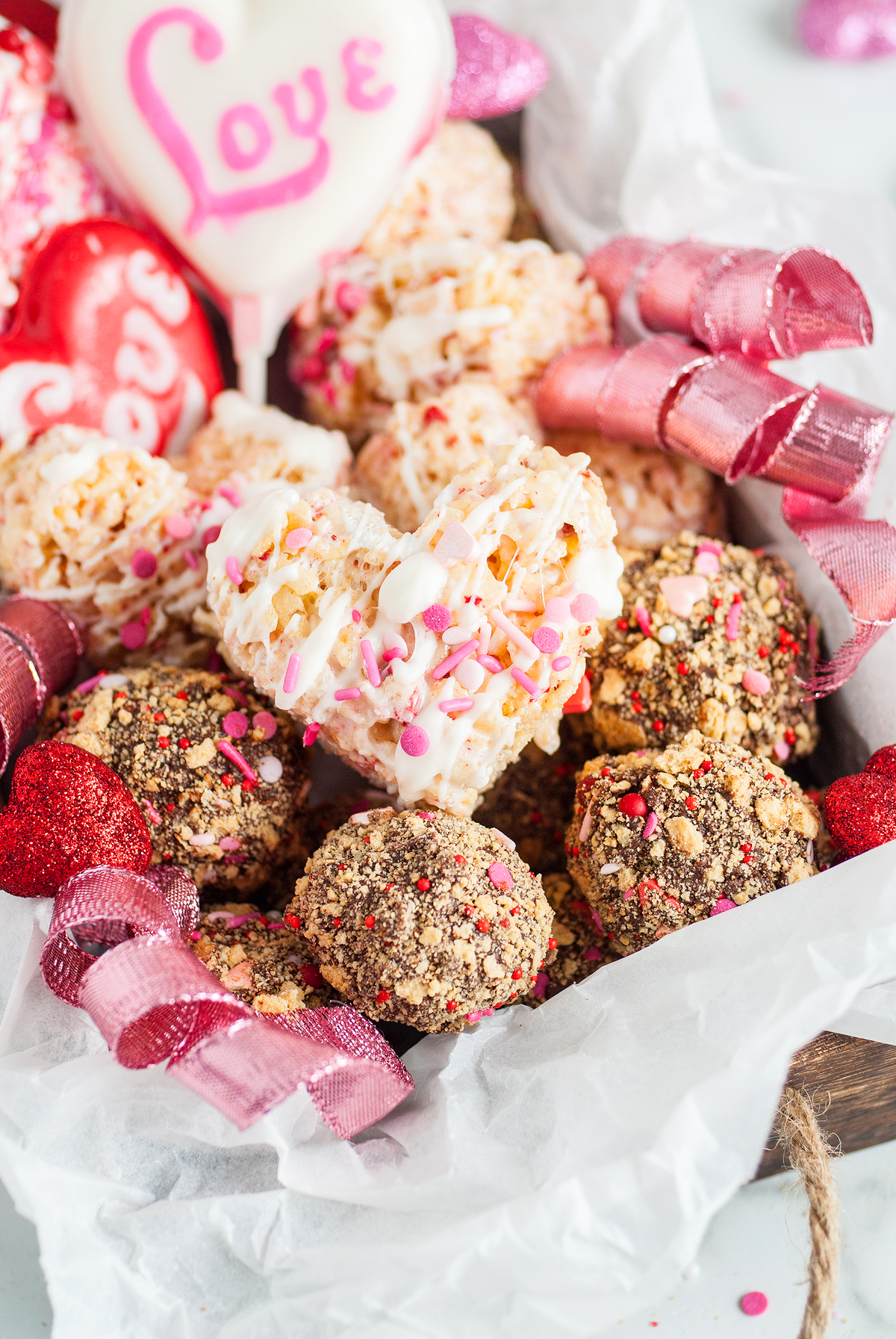 Assorted heart-shaped and round homemade Valentine’s treats with pink ribbons and a “Love” heart lollipop—perfect for your Valentine's Day Homemade Treat Box or to inspire easy recipes at home.