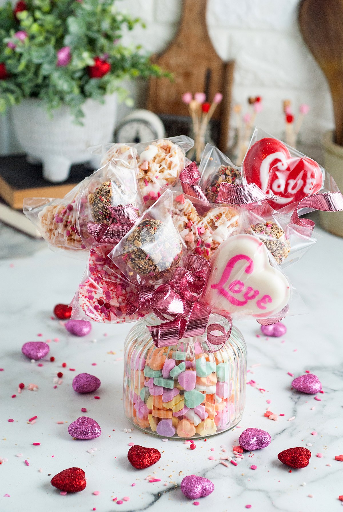 A glass jar of candy hearts sits beside a charming valentine treat box filled with pink ribbon-wrapped Valentine treats and heart-shaped cookies.
