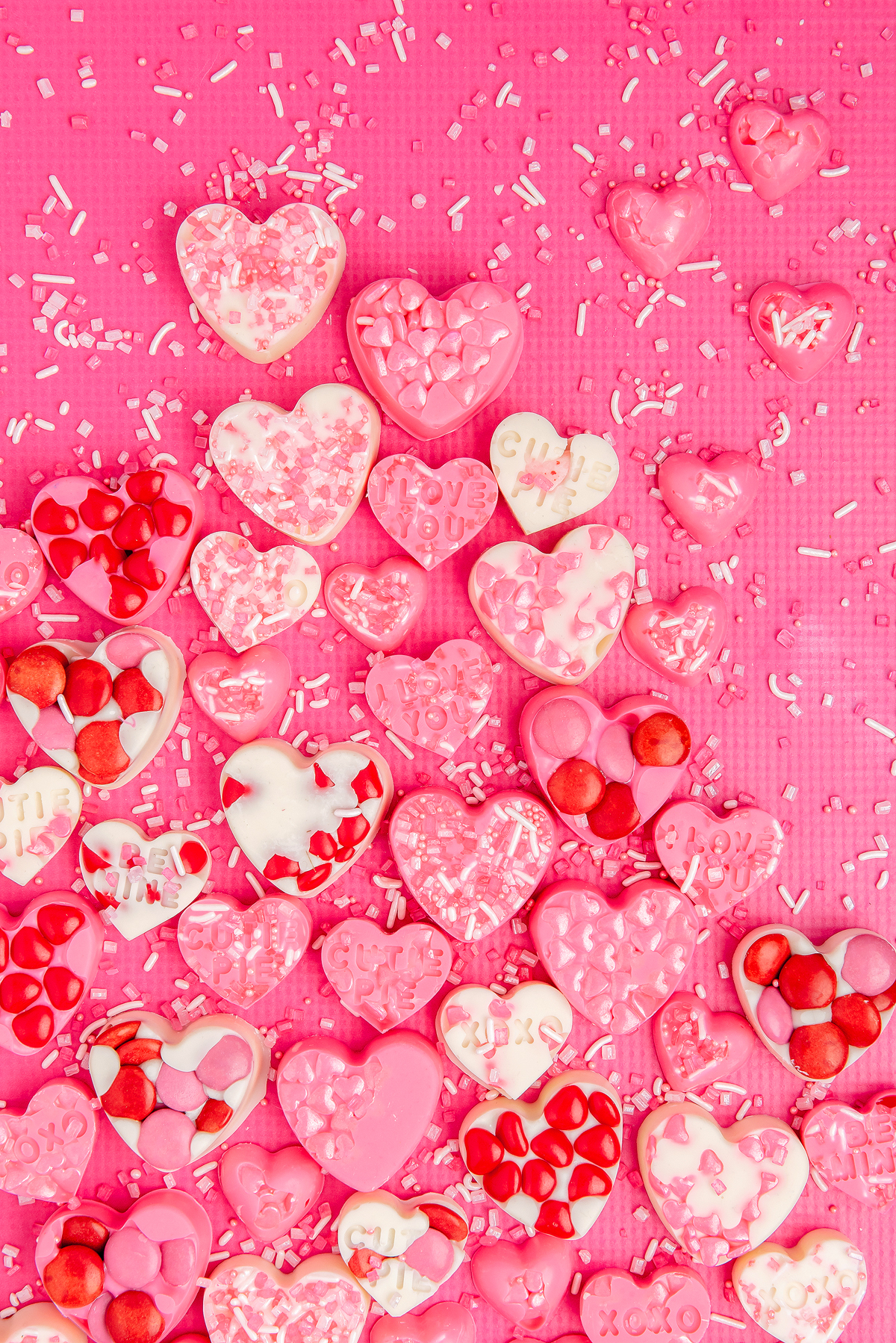 Heart-shaped pink and white homemade Valentine's candy with sprinkles scattered on a pink background.