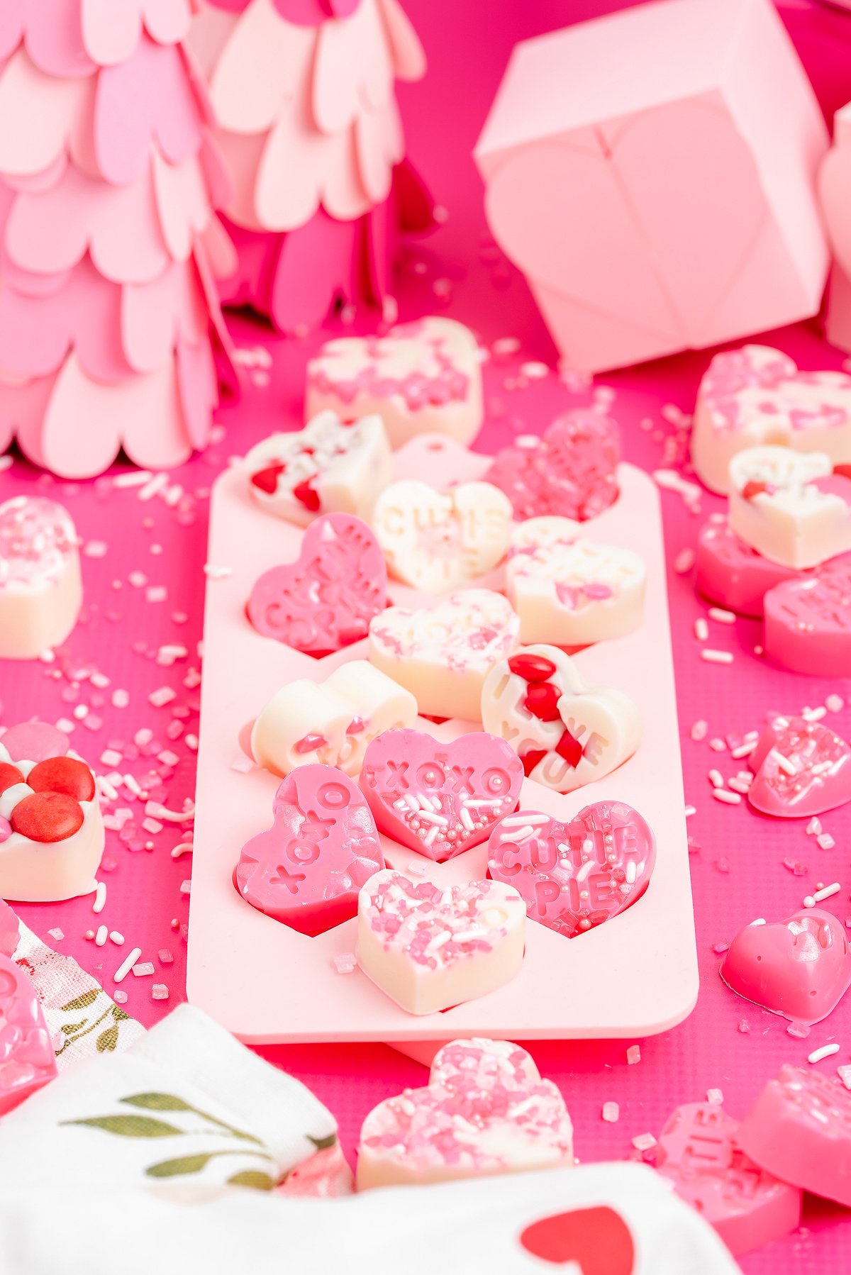 A tray of pink and white heart-shaped candies with sprinkles on a bright pink background—perfect easy Valentine's treats or homemade valentine's candy delights.