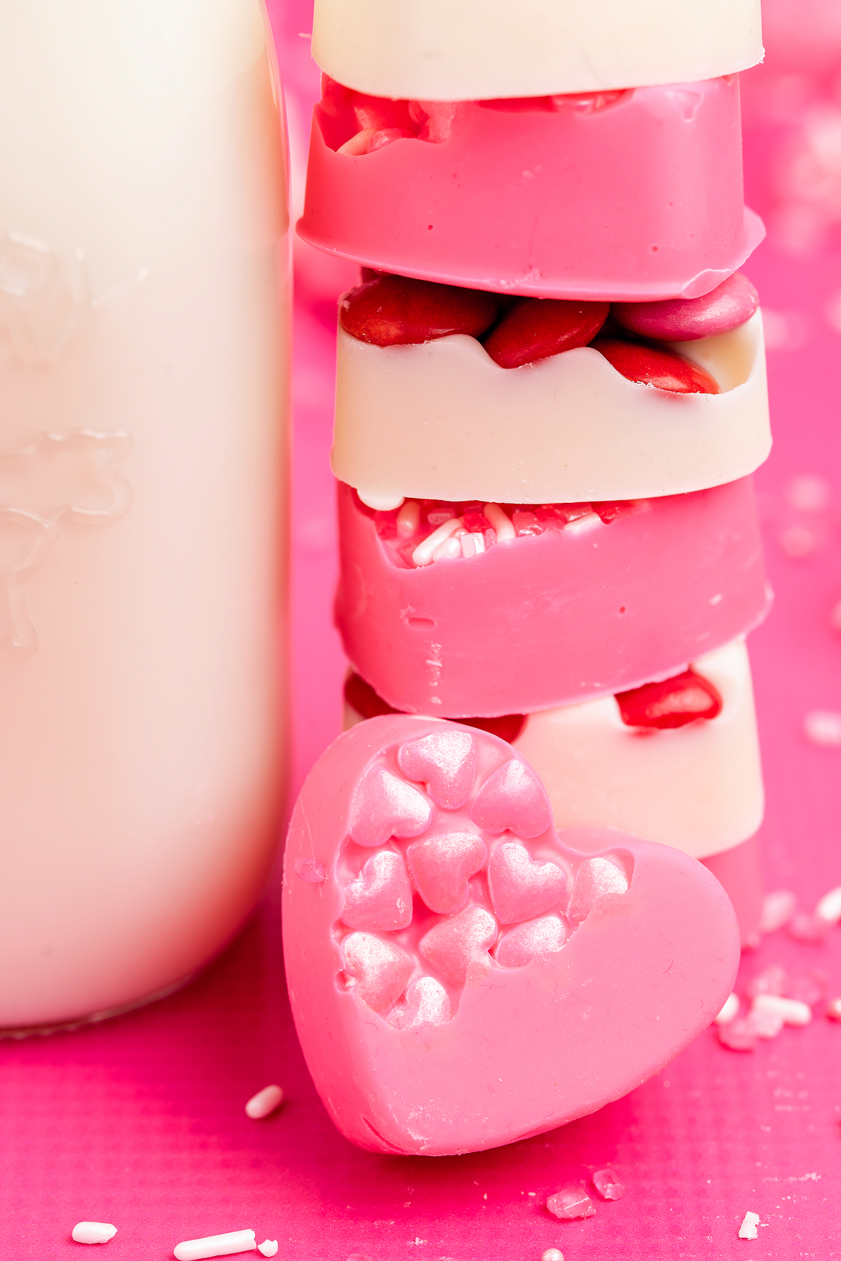 Stack of pink and white heart-shaped candies with a heart candy in front on a pink surface, perfect for easy Valentine's treats or gifting as homemade valentine's candy.
