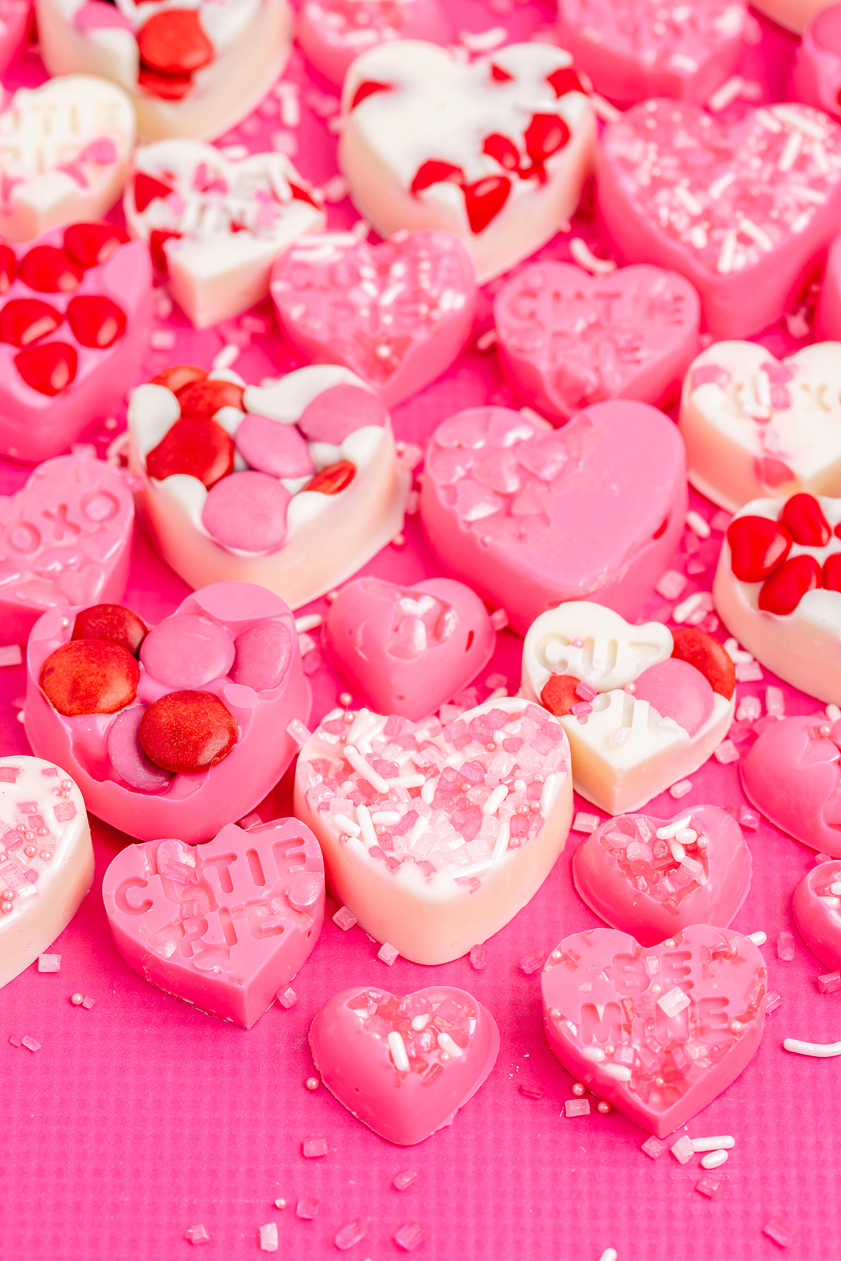 Assorted pink and white heart-shaped candies with sprinkles and decorations on a pink background—perfect as easy Valentine's treats or inspiration for homemade Valentine's candy.