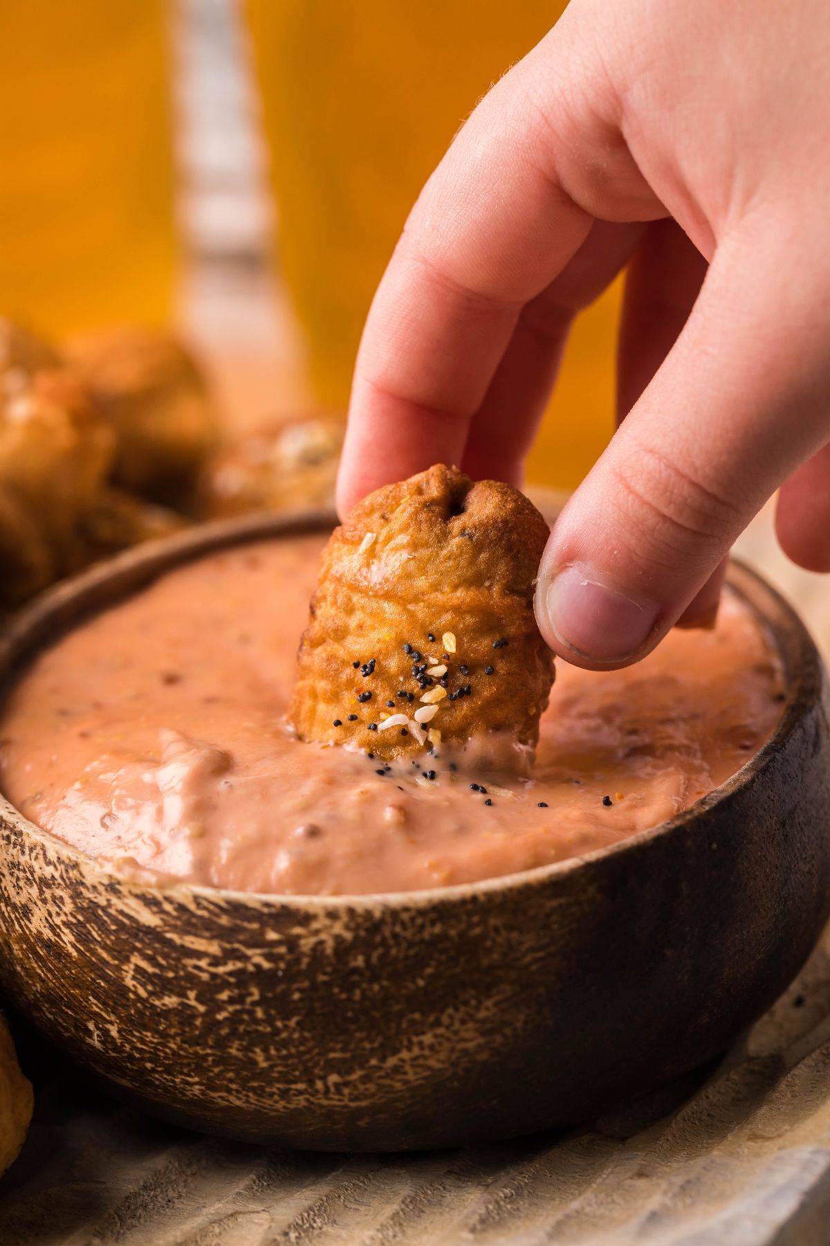 A hand dips a nugget topped with seasoning into a bowl of creamy pink Easy Horseradish Mayo Dipping Sauce—ideal for game day appys or pairing with beer battered little smokies.