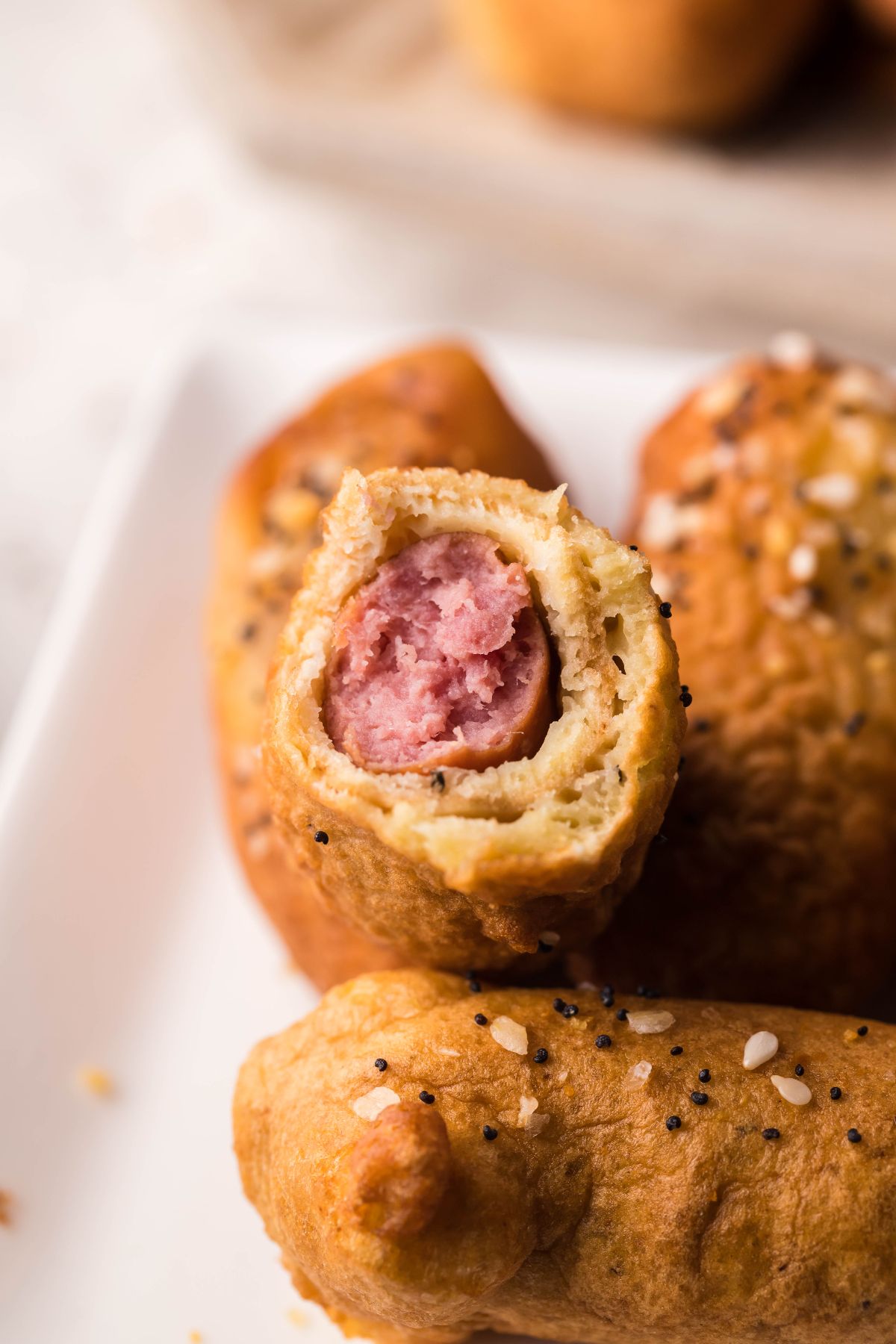 A close-up of a beer battered little smokies corndog with a bite taken out, showing the sausage inside and sprinkled seeds on top—perfect as an appetizer or finger food.