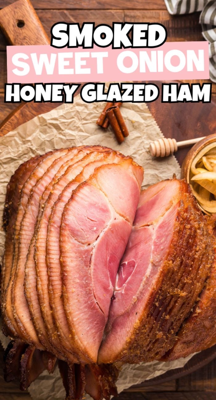 Sliced Smoked Honey Glazed Ham on parchment with cinnamon sticks and a honey dipper, arranged on a wooden table.