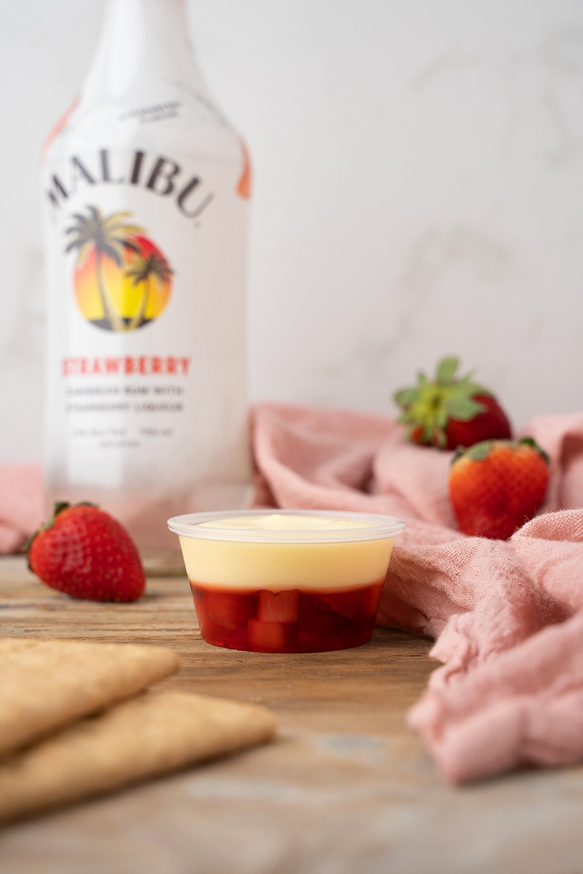 A dessert cup with fruit and cream, strawberries, and a Malibu Strawberry bottle in the background—perfect for serving cheesecake shooters or pairing with strawberry flavoured rum.