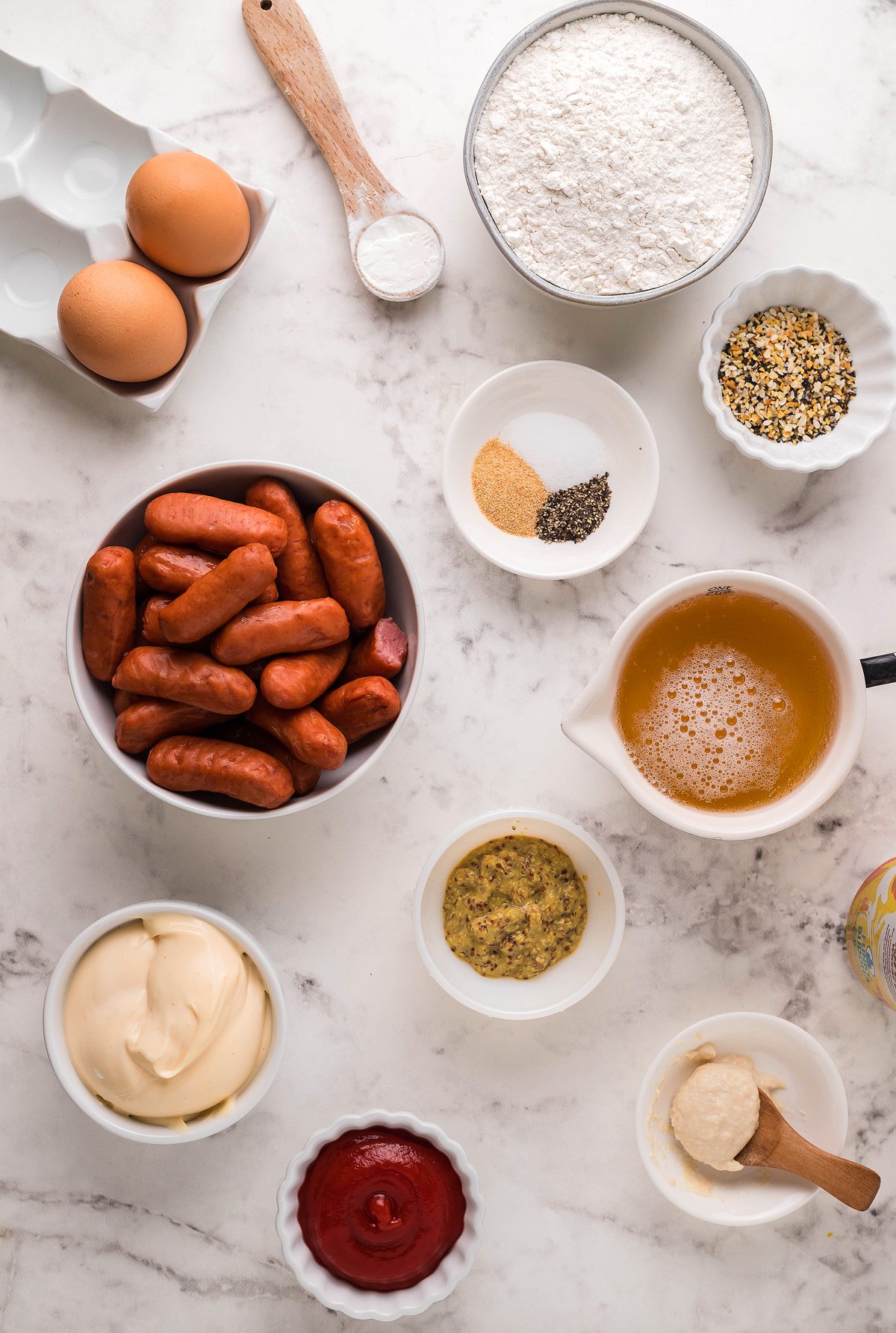Assorted ingredients on a marble surface, including eggs, flour, spices, broth, and sauces in bowls—perfect for making game day appy favorites like cocktail weenies or beer battered little smokies.