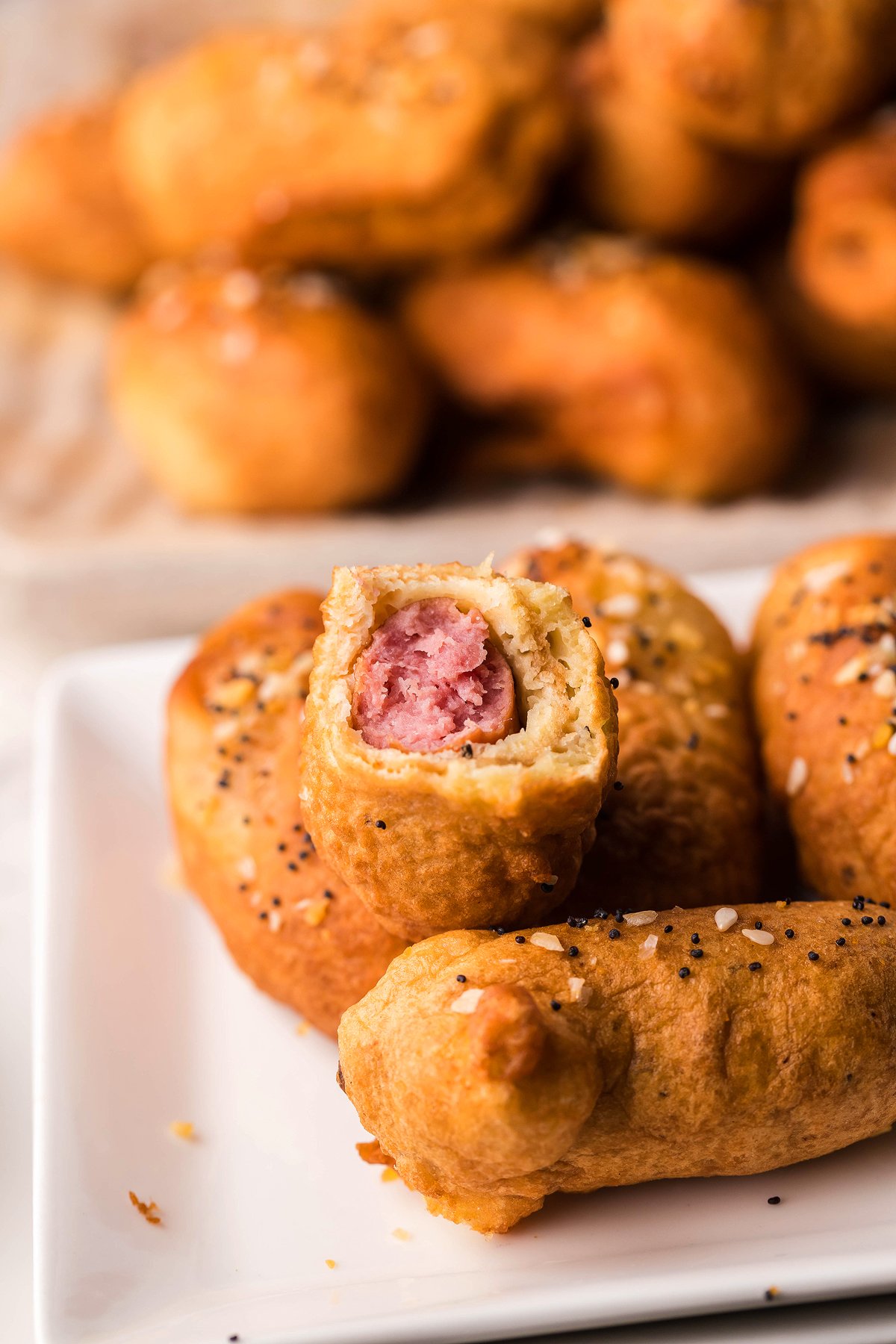 Two pigs in a blanket on a plate, one with a bite showing sausage inside the golden pastry—perfect as a game day appy, especially when served with easy horseradish mayo dipping sauce.