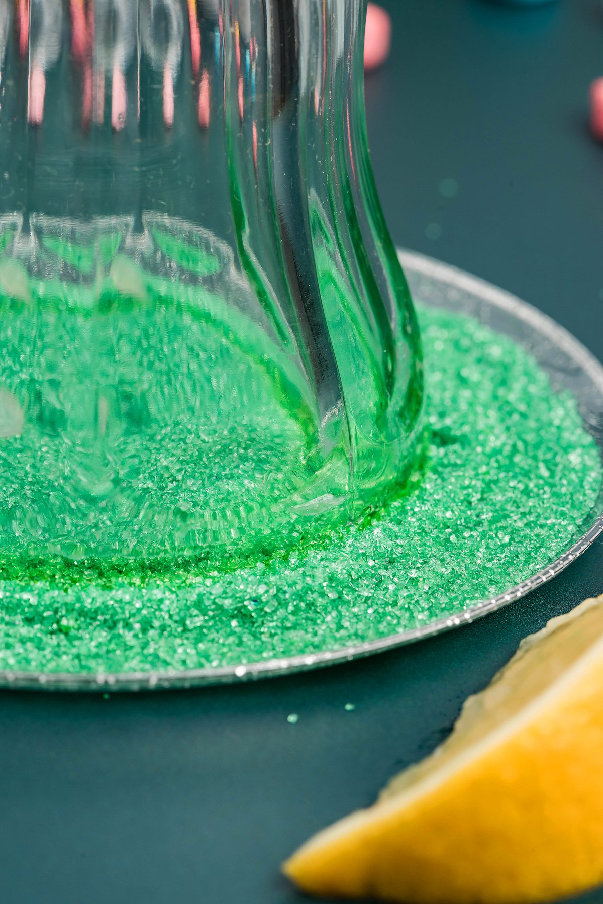 A glass rim dipped in green sugar crystals hints at a festive treat—perfect for serving a boozy shamrock shake, with a lemon wedge nearby on a dark surface.