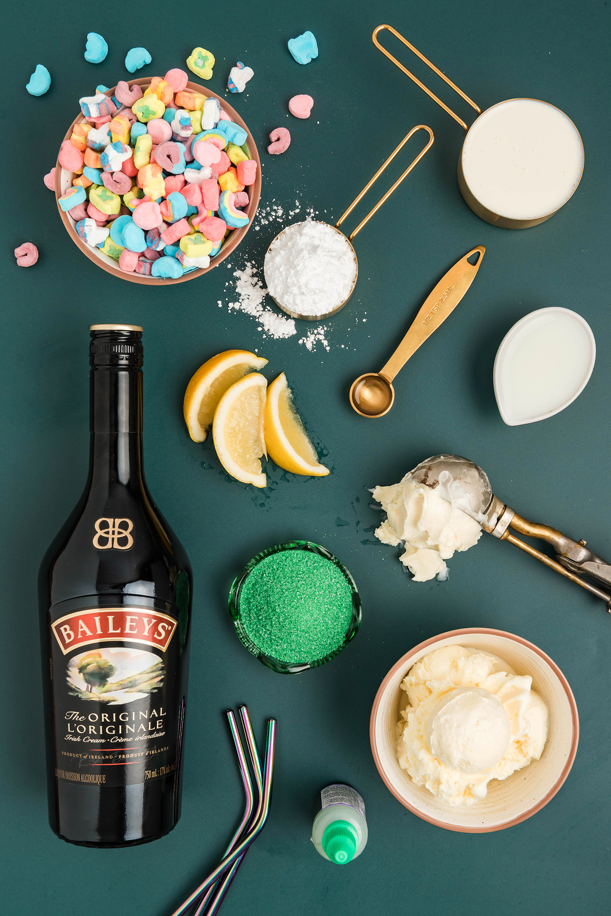 Baileys, ice cream, Lucky Charms cereal, milk, cream, lemons, powdered sugar, and baking tools come together on a green background—perfect ingredients for a festive Irish cream milkshake or boozy shamrock shake.