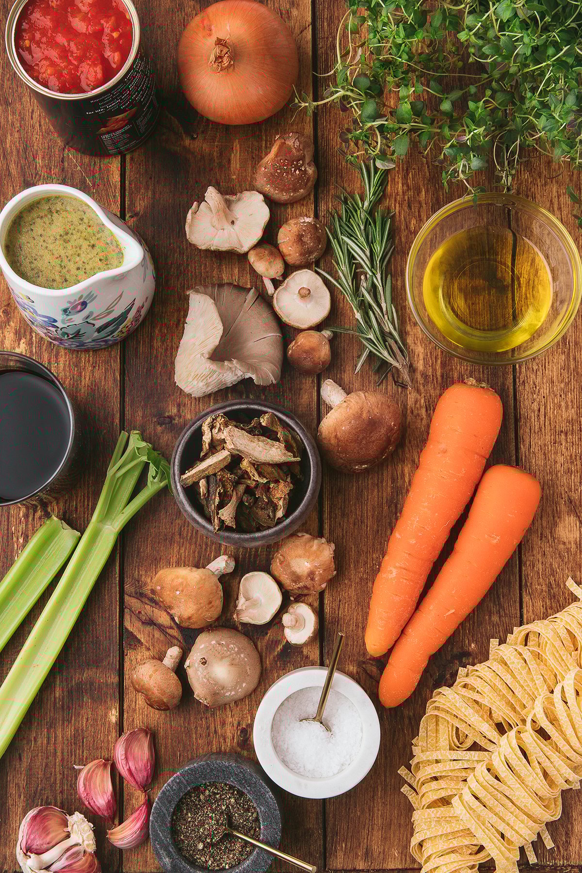 Assorted vegetables, herbs, pasta, and seasonings arranged on a rustic wooden table, perfect for preparing a flavorful meatless ragu or mushroom ragu, viewed from above.